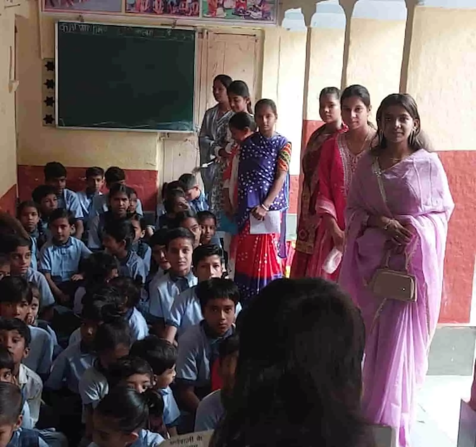 तस्वीर में आंचलिक स्कूल के कमरे में शिक्षिकाएं खड़ी हैं और यूनिफॉर्म पहने विद्यार्थी जमीन पर बैठे हैं। तस्वीर में आंचलिक स्कूल के कमरे में शिक्षिकाएं खड़ी हैं और यूनिफॉर्म पहने विद्यार्थी जमीन पर बैठे हैं।