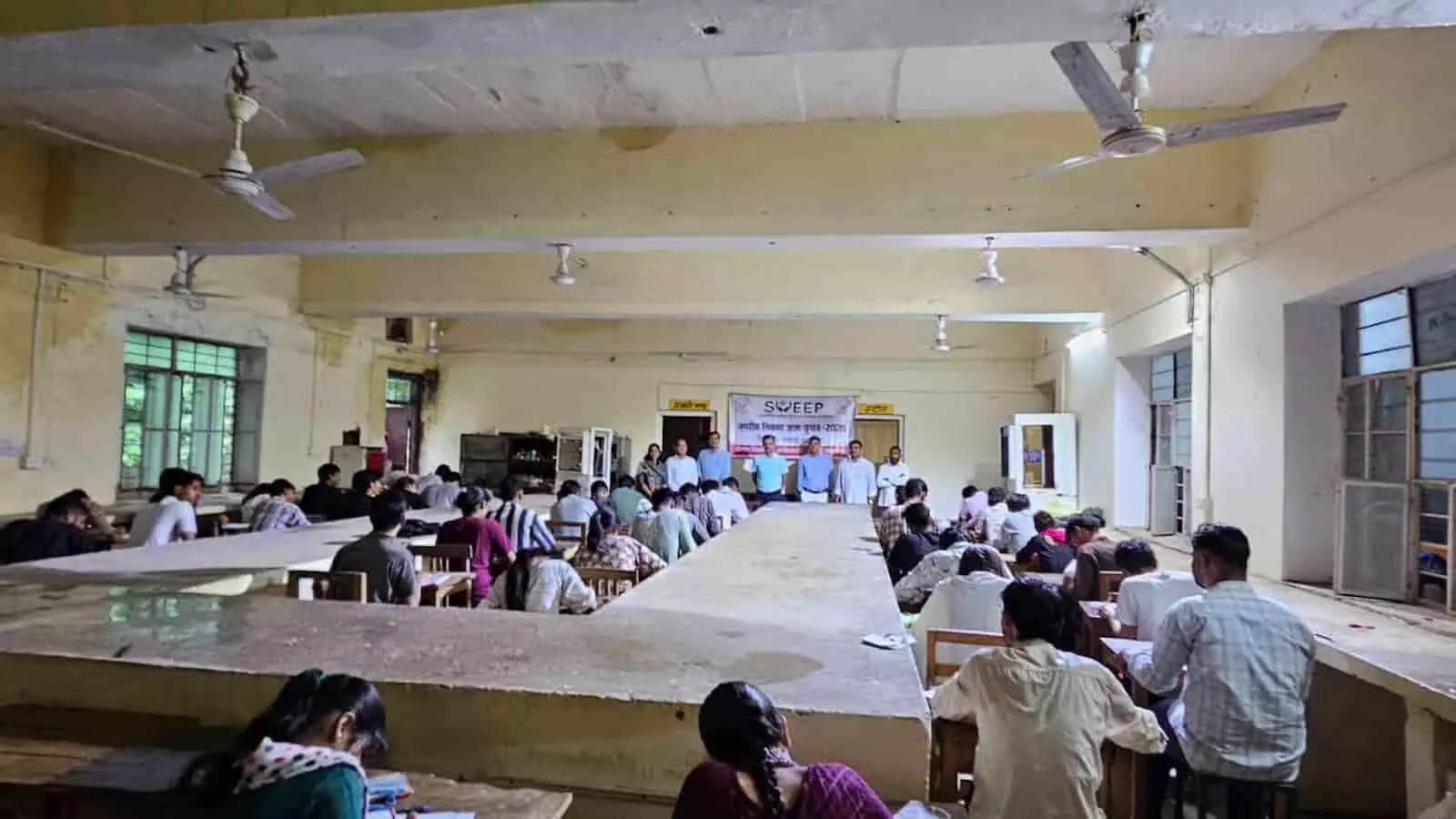 तस्वीर में महाविद्यालय के कमरे में डेस्क पर बैठे विद्यार्थी निबंध प्रतियोगिता में लिखते दिख रहे हैं। तस्वीर में महाविद्यालय के कमरे में डेस्क पर बैठे विद्यार्थी निबंध प्रतियोगिता में लिखते दिख रहे हैं।