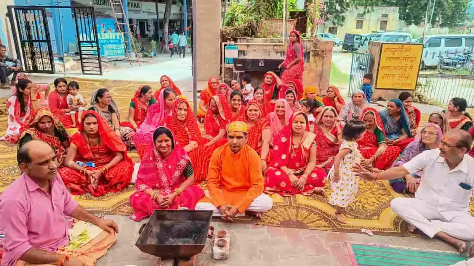 तस्वीर में हवन कुंड के पास बैठे श्रद्धालु और पीछे लाल साड़ियों में महिलाएं पूजा कर रही हैं। तस्वीर में हवन कुंड के पास बैठे श्रद्धालु और पीछे लाल साड़ियों में महिलाएं पूजा कर रही हैं।