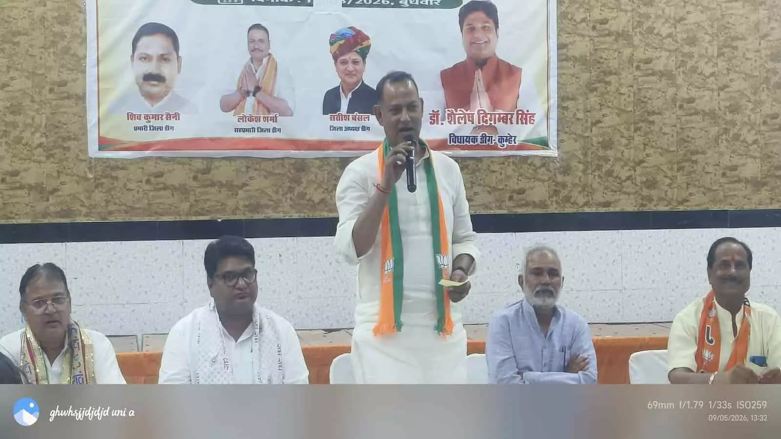 तस्वीर में बैठे हुए चार पुरुषों के बीच खड़े होकर एक नेता भाषण दे रहे हैं। तस्वीर में बैठे हुए चार पुरुषों के बीच खड़े होकर एक नेता भाषण दे रहे हैं।