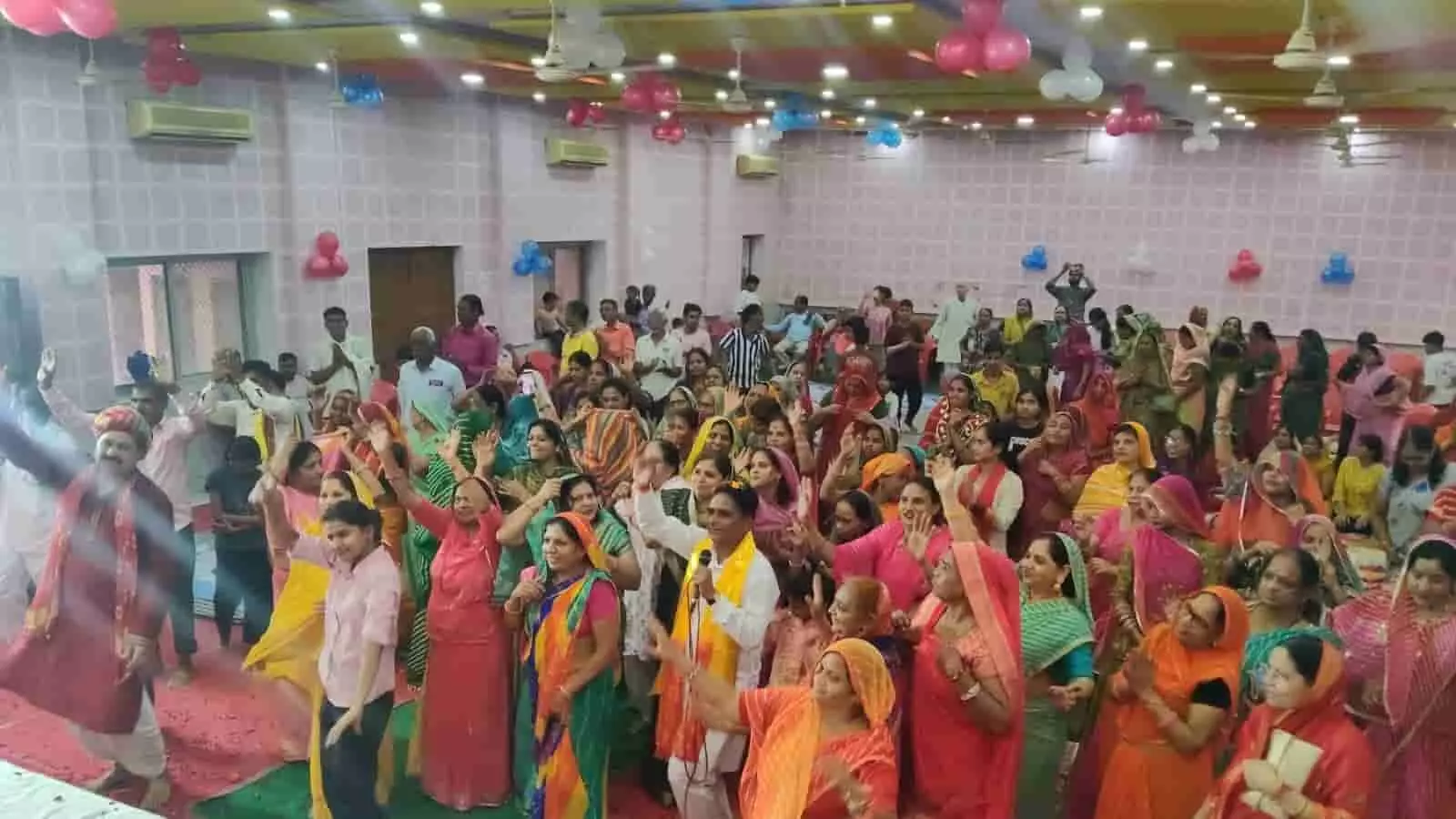 तस्वीर में सजे हॉल में अनेक लोग हाथ उठाकर भक्ति गीतों पर नाच रहे हैं। तस्वीर में सजे हॉल में अनेक लोग हाथ उठाकर भक्ति गीतों पर नाच रहे हैं।