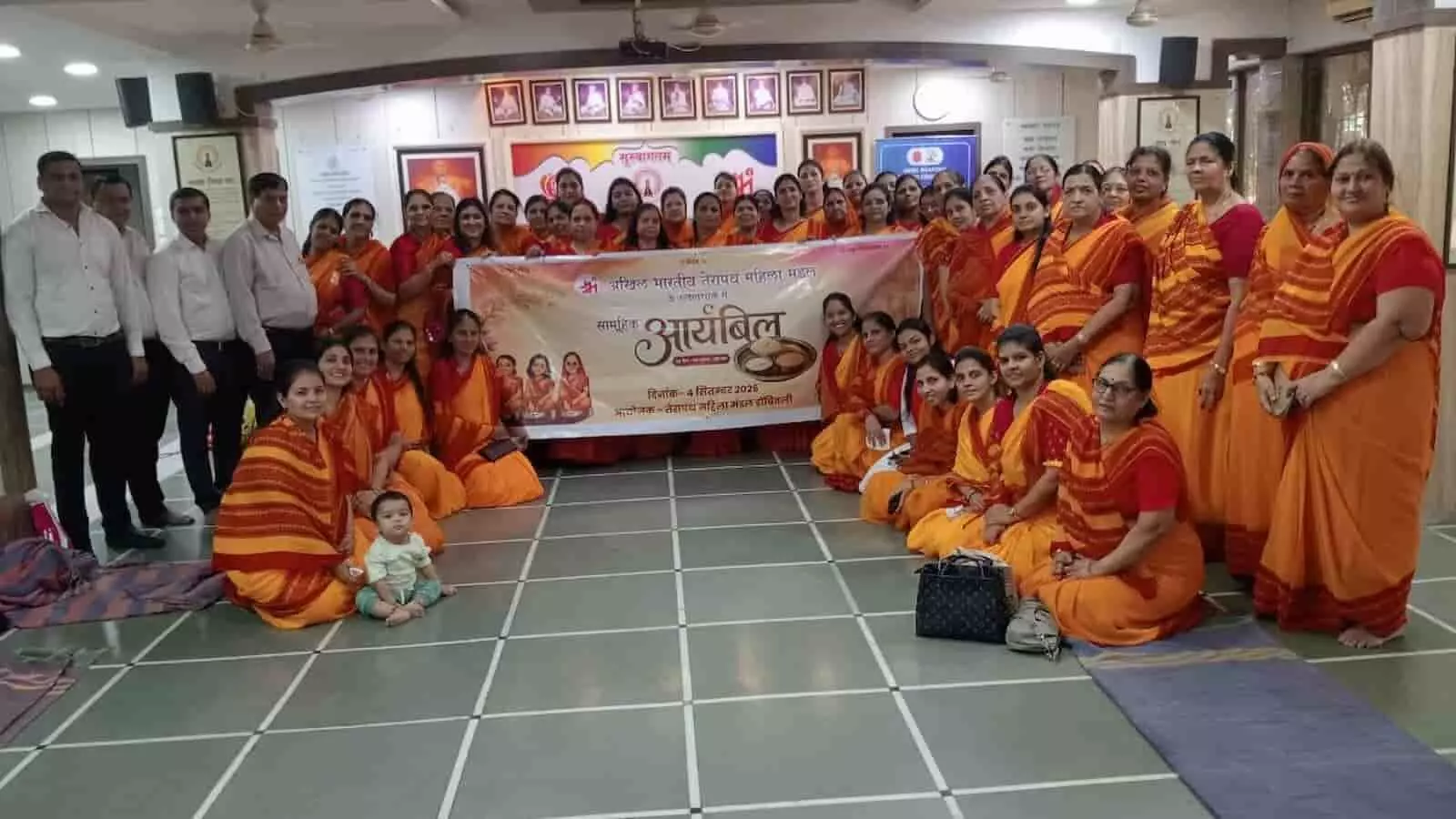 तस्वीर में बाईं ओर पुरुष खड़े हैं और केंद्र में महिलाएं बैनर लेकर समूह में बैठी हैं। तस्वीर में बाईं ओर पुरुष खड़े हैं और केंद्र में महिलाएं बैनर लेकर समूह में बैठी हैं।