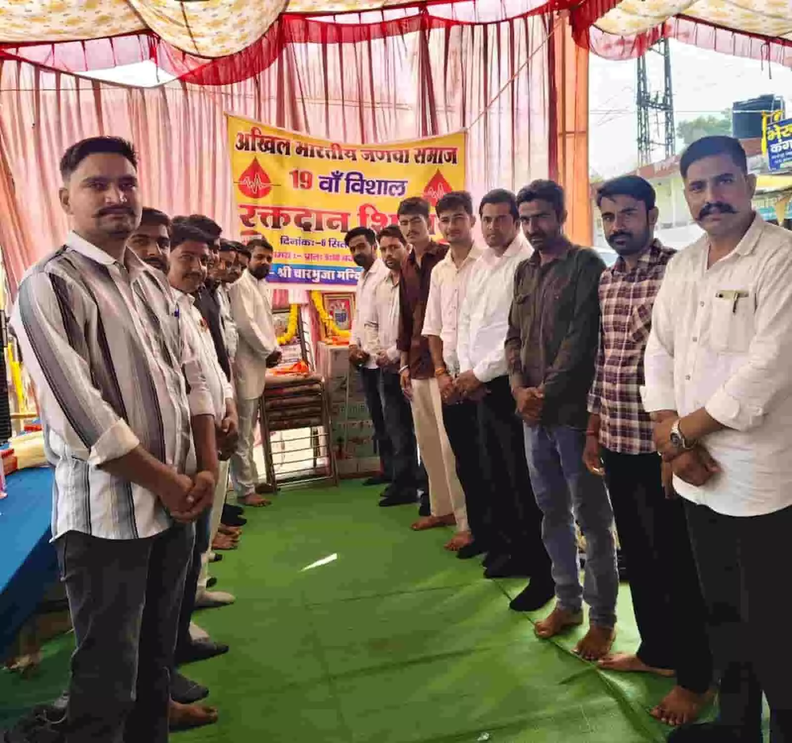तस्वीर में दिख रही एक पंडाल में बैनर के सामने खड़े कई पुरुषों की पंक्ति। तस्वीर में दिख रही एक पंडाल में बैनर के सामने खड़े कई पुरुषों की पंक्ति।
