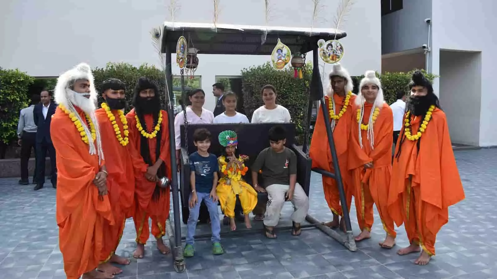 तस्वीर में दिख रही झांकी में साधु की पोशाक पहने लोग और बच्चे झूले के पास खड़े हैं। तस्वीर में दिख रही झांकी में साधु की पोशाक पहने लोग और बच्चे झूले के पास खड़े हैं।