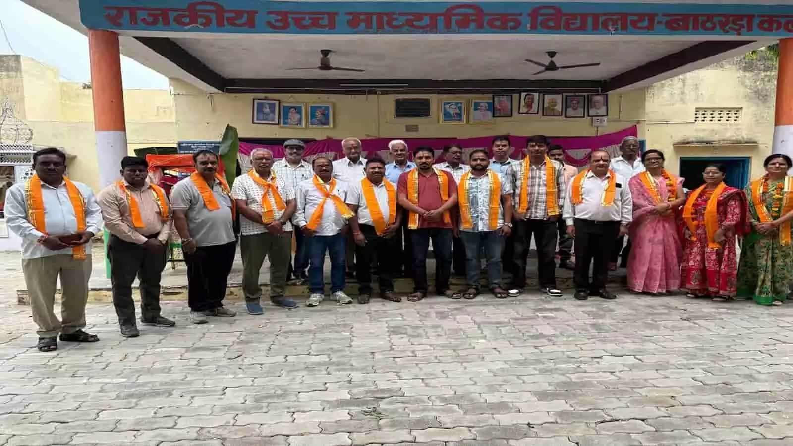 तस्वीर में केसरिया उपरणा पहने कई लोग स्कूल की इमारत के सामने एक साथ कतार में खड़े हैं। तस्वीर में केसरिया उपरणा पहने कई लोग स्कूल की इमारत के सामने एक साथ कतार में खड़े हैं।