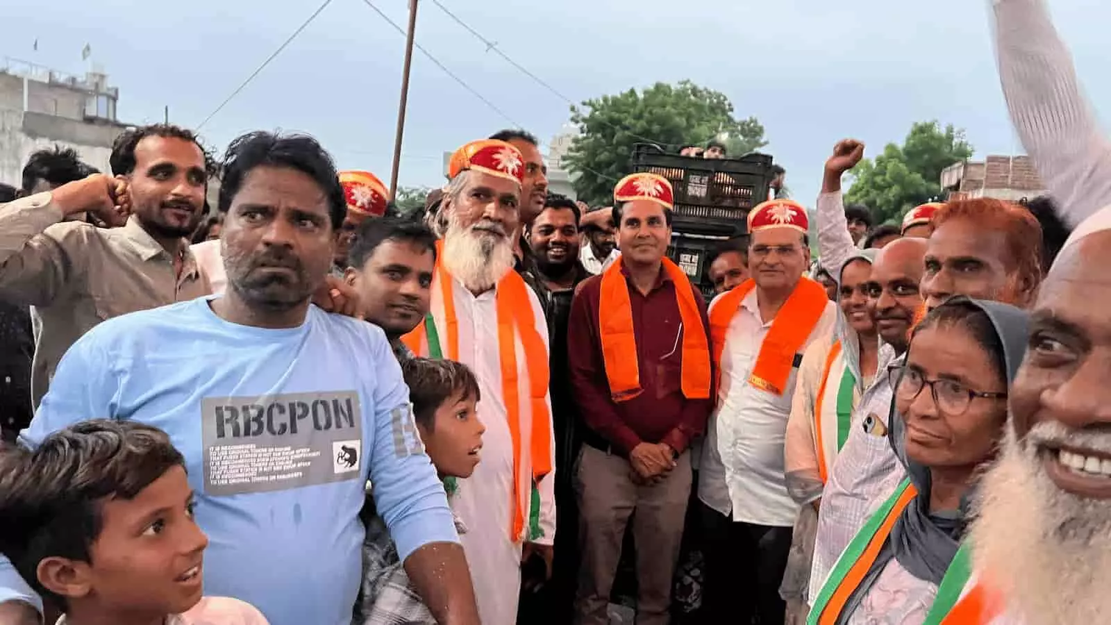 तस्वीर में बाएं नीली शर्ट वाला युवक, बीच में सफेद दाढ़ी वाले बुजुर्ग और समर्थक खड़े हैं। तस्वीर में बाएं नीली शर्ट वाला युवक, बीच में सफेद दाढ़ी वाले बुजुर्ग और समर्थक खड़े हैं।