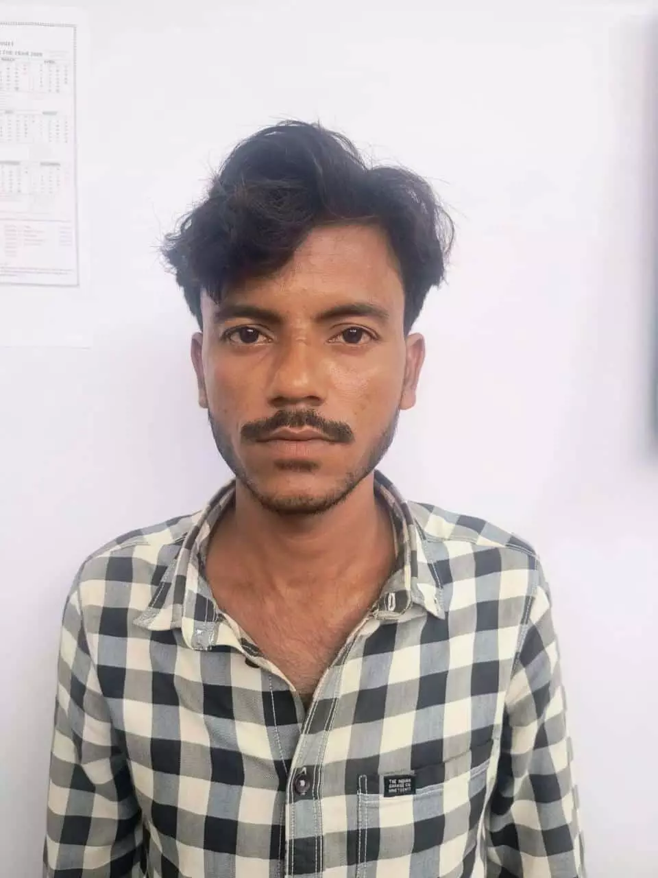 तस्वीर में मूंछों वाला व्यक्ति सफेद दीवार के पास खड़े होकर सीधे देख रहा है। तस्वीर में मूंछों वाला व्यक्ति सफेद दीवार के पास खड़े होकर सीधे देख रहा है।