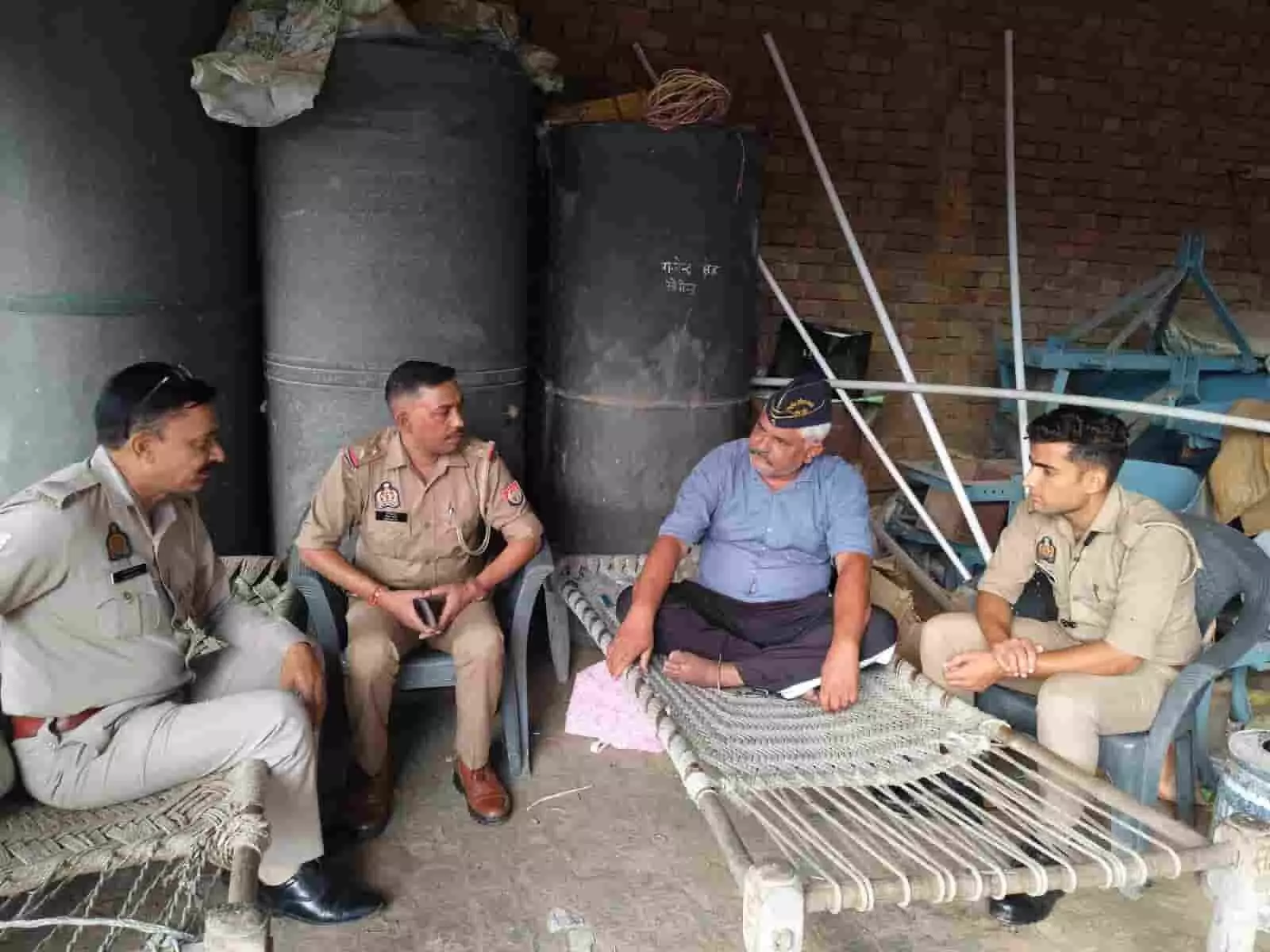 तस्वीर में दिख रही जगह पर तीन पुलिसकर्मी खाट पर बैठे एक व्यक्ति से बात कर रहे हैं। तस्वीर में दिख रही जगह पर तीन पुलिसकर्मी खाट पर बैठे एक व्यक्ति से बात कर रहे हैं।