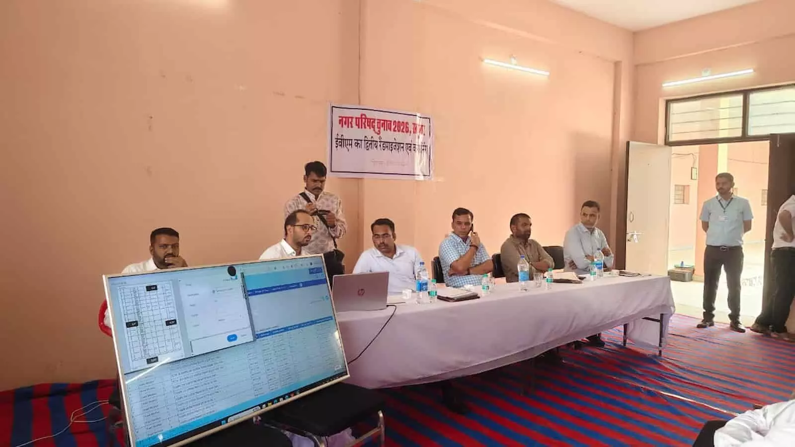 तस्वीर में दिख रही एक मेज पर अधिकारी बैठे हैं और सामने कंप्यूटर स्क्रीन मौजूद है। तस्वीर में दिख रही एक मेज पर अधिकारी बैठे हैं और सामने कंप्यूटर स्क्रीन मौजूद है।