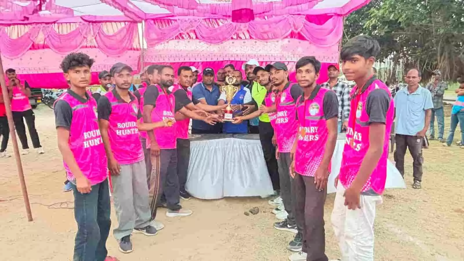 तस्वीर में दिख रही क्रिकेट टीम के खिलाड़ी मैदान में गुलाबी टी-शर्ट पहनकर ट्रॉफी के साथ खड़े हैं। तस्वीर में दिख रही क्रिकेट टीम के खिलाड़ी मैदान में गुलाबी टी-शर्ट पहनकर ट्रॉफी के साथ खड़े हैं।