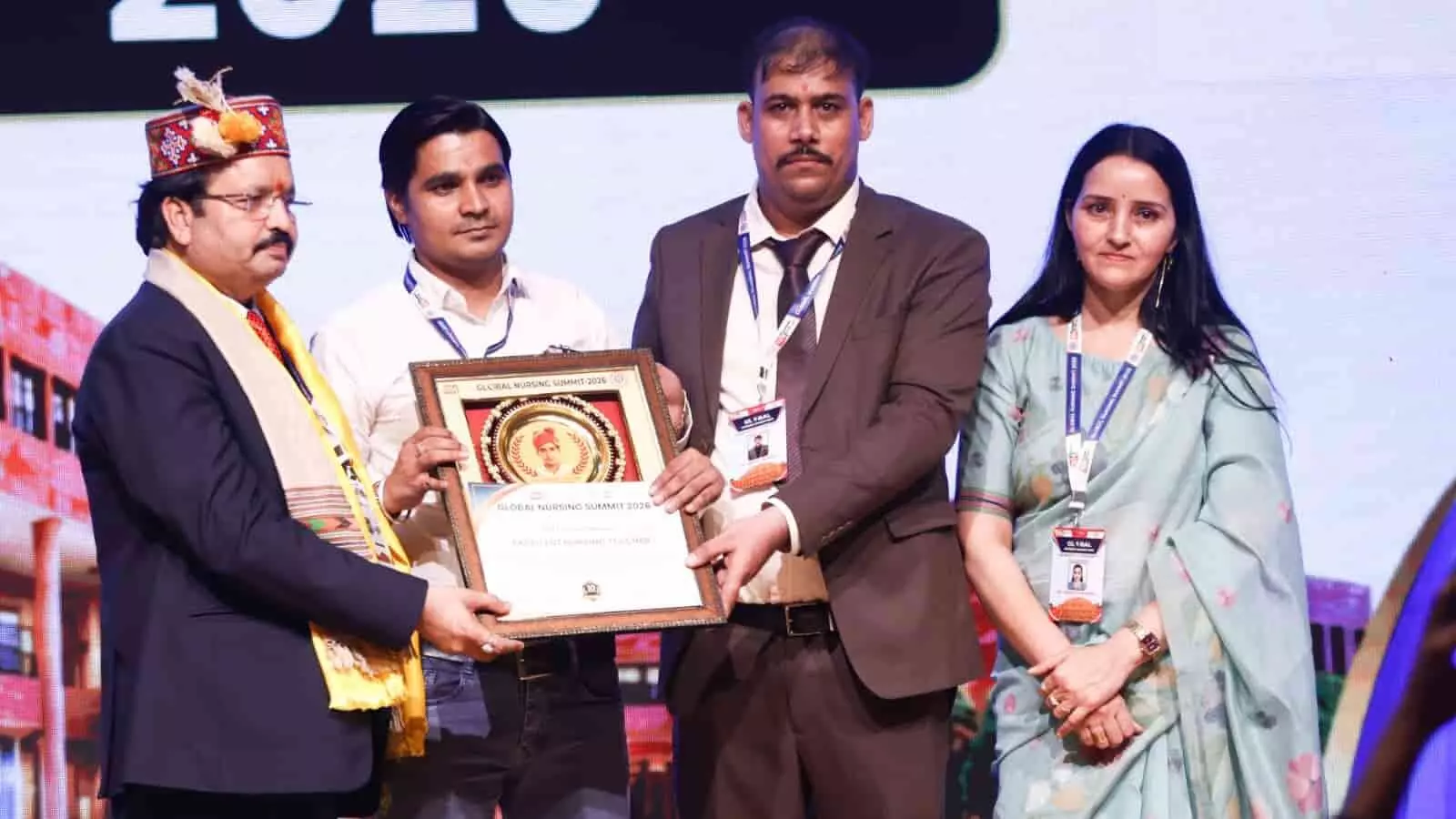 तस्वीर में चार लोग मंच पर खड़े होकर एक फ्रेम किया हुआ सम्मान पत्र थामे हुए हैं। तस्वीर में चार लोग मंच पर खड़े होकर एक फ्रेम किया हुआ सम्मान पत्र थामे हुए हैं।