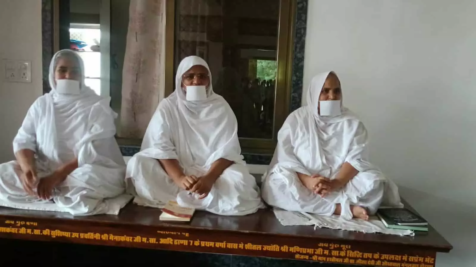 तस्वीर में तीन जैन साध्वियां मुंह पर मुखपट्टी बांधकर आसन पर बैठी हुई दिख रही हैं। तस्वीर में तीन जैन साध्वियां मुंह पर मुखपट्टी बांधकर आसन पर बैठी हुई दिख रही हैं।