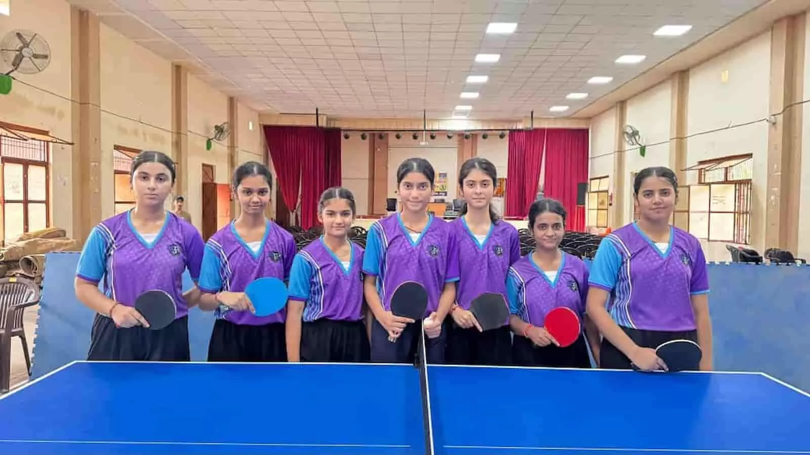 तस्वीर में दिख रही सात लड़कियां स्पोर्ट्स जर्सी पहने टेबल टेनिस बैट लेकर खड़ी हैं। तस्वीर में दिख रही सात लड़कियां स्पोर्ट्स जर्सी पहने टेबल टेनिस बैट लेकर खड़ी हैं।