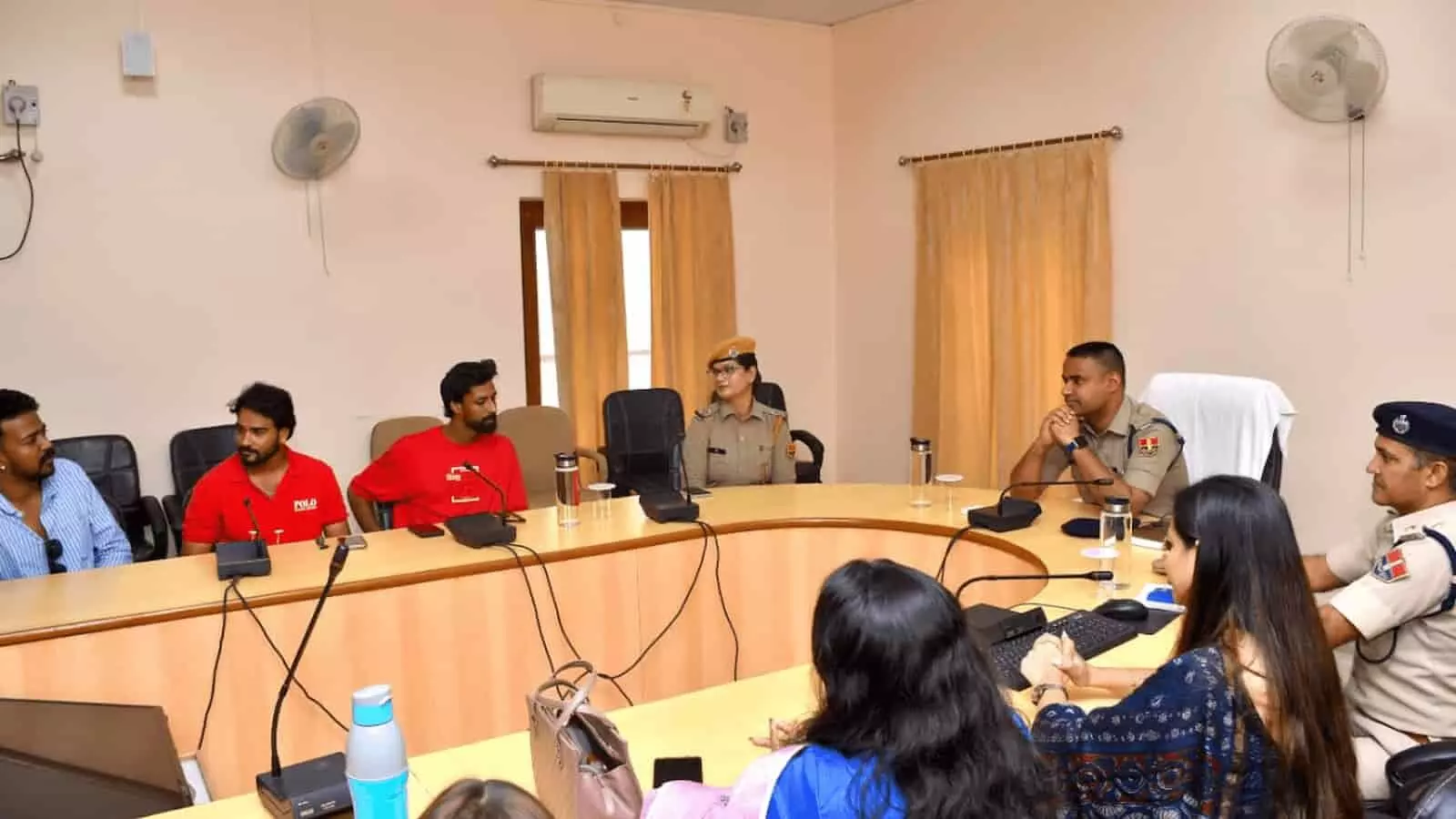 तस्वीर में बाईं ओर नागरिक और दाईं ओर वर्दीधारी पुलिस अधिकारी एक गोल मेज पर बैठे हैं। तस्वीर में बाईं ओर नागरिक और दाईं ओर वर्दीधारी पुलिस अधिकारी एक गोल मेज पर बैठे हैं।