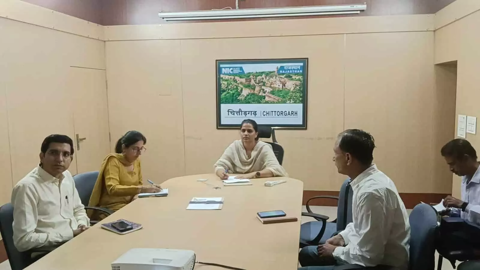 तस्वीर में दिख रहे अधिकारी कमरे में मेज के चारों ओर बैठकर दस्तावेजों को देख रहे हैं। तस्वीर में दिख रहे अधिकारी कमरे में मेज के चारों ओर बैठकर दस्तावेजों को देख रहे हैं।