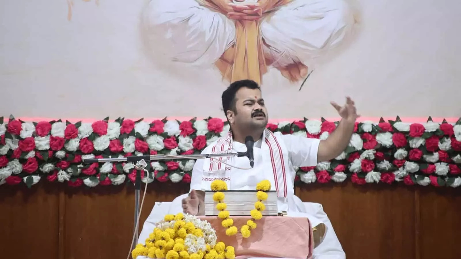 तस्वीर में दिख रहे वक्ता सफेद वस्त्र पहनकर फूलों से सजे मंच पर संबोधन दे रहे हैं। तस्वीर में दिख रहे वक्ता सफेद वस्त्र पहनकर फूलों से सजे मंच पर संबोधन दे रहे हैं।