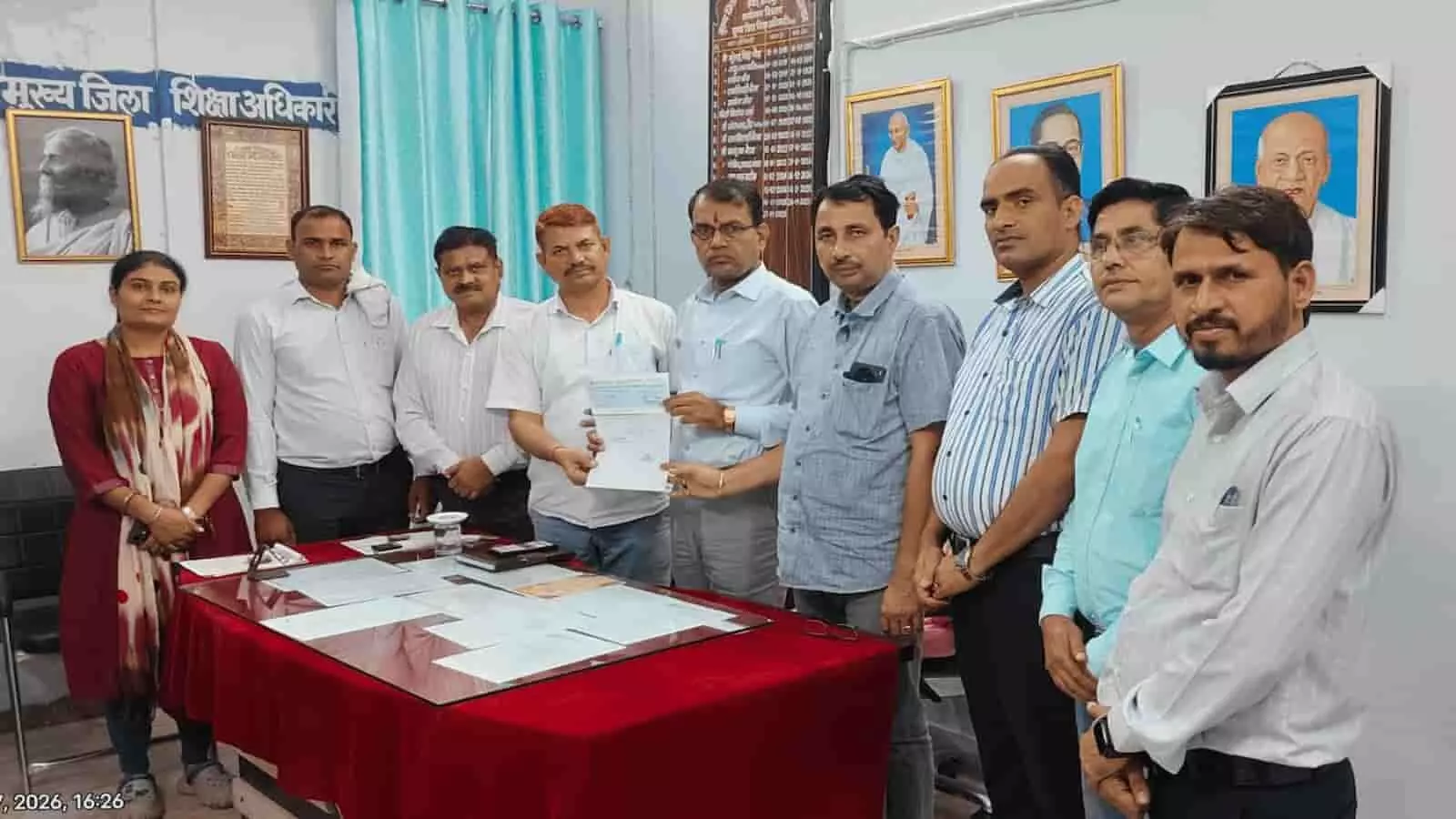 तस्वीर में दिख रहे लोग कार्यालय में खड़े होकर एक चेक पकड़े हुए हैं। तस्वीर में दिख रहे लोग कार्यालय में खड़े होकर एक चेक पकड़े हुए हैं।