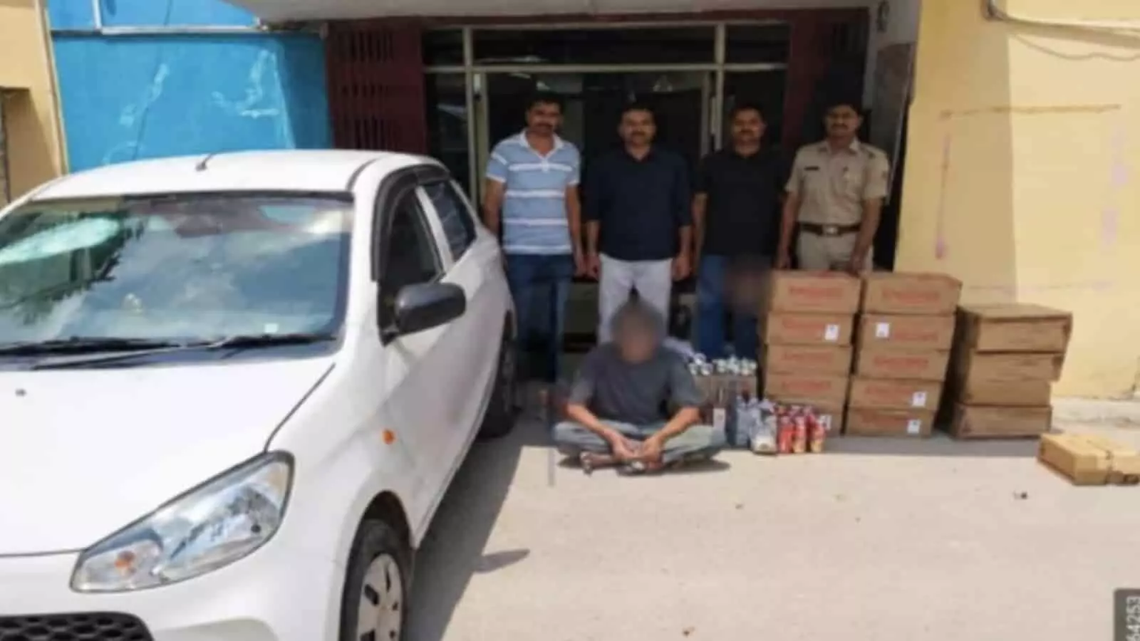 तस्वीर में सफेद कार के पास खड़े पुलिसकर्मी और शराब के कार्टन दिख रहे हैं। तस्वीर में सफेद कार के पास खड़े पुलिसकर्मी और शराब के कार्टन दिख रहे हैं।