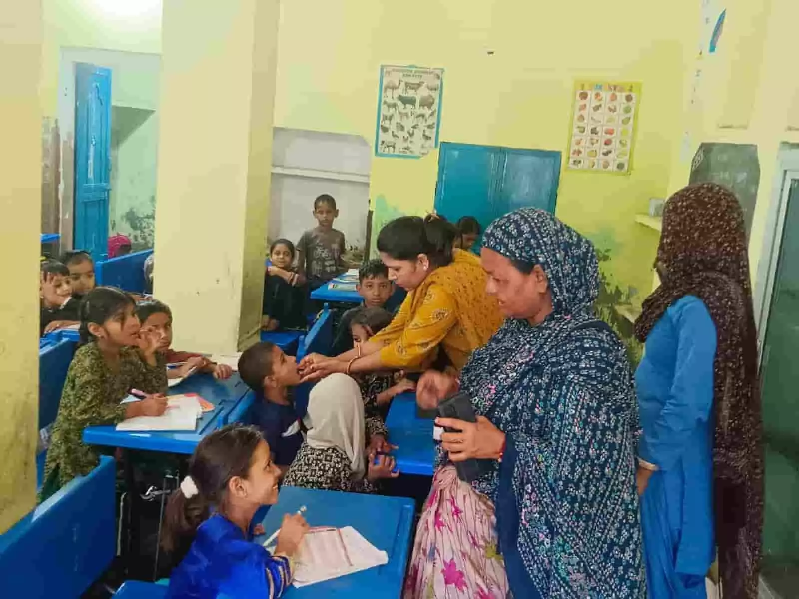 तस्वीर में दिख रही एक स्वास्थ्य कर्मी स्कूल के कमरे में बैठे बच्चे को दवा दे रही है। तस्वीर में दिख रही एक स्वास्थ्य कर्मी स्कूल के कमरे में बैठे बच्चे को दवा दे रही है।