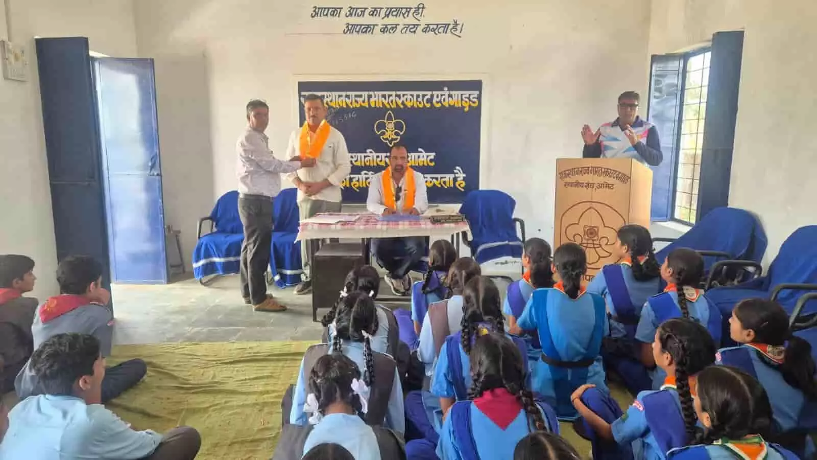 तस्वीर में अधिकारी मंच पर खड़े होकर जमीन पर बैठे स्काउट गाइड छात्रों को संबोधित कर रहे हैं। तस्वीर में अधिकारी मंच पर खड़े होकर जमीन पर बैठे स्काउट गाइड छात्रों को संबोधित कर रहे हैं।
