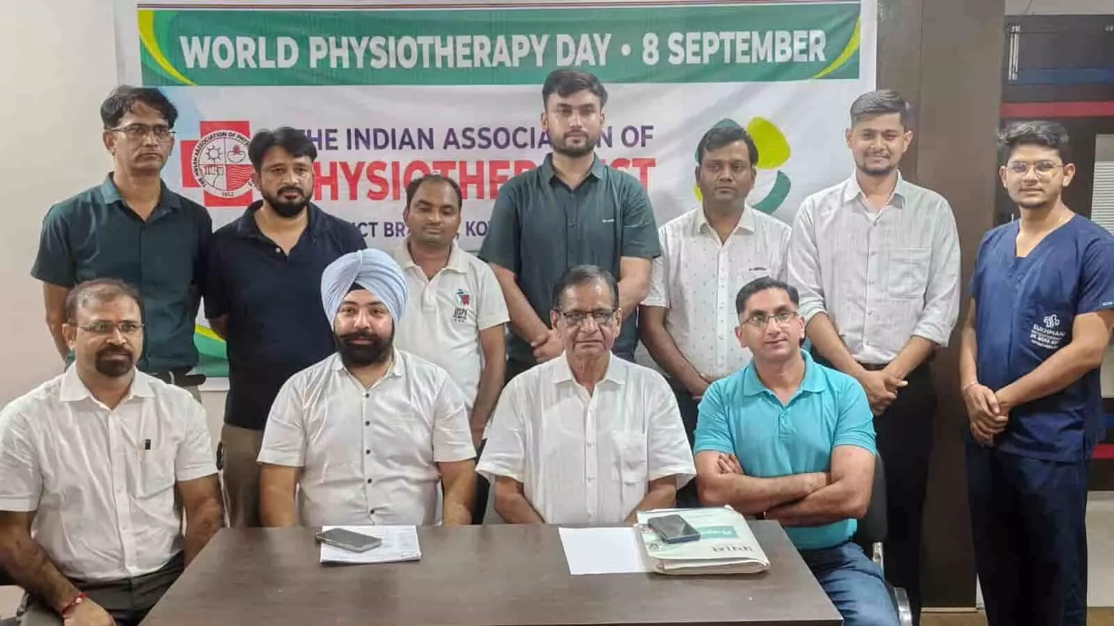 तस्वीर में मेज के पीछे बैठे और खड़े पुरुष विश्व फिजियोथेरेपी दिवस का बैनर प्रदर्शित कर रहे हैं। तस्वीर में मेज के पीछे बैठे और खड़े पुरुष विश्व फिजियोथेरेपी दिवस का बैनर प्रदर्शित कर रहे हैं।