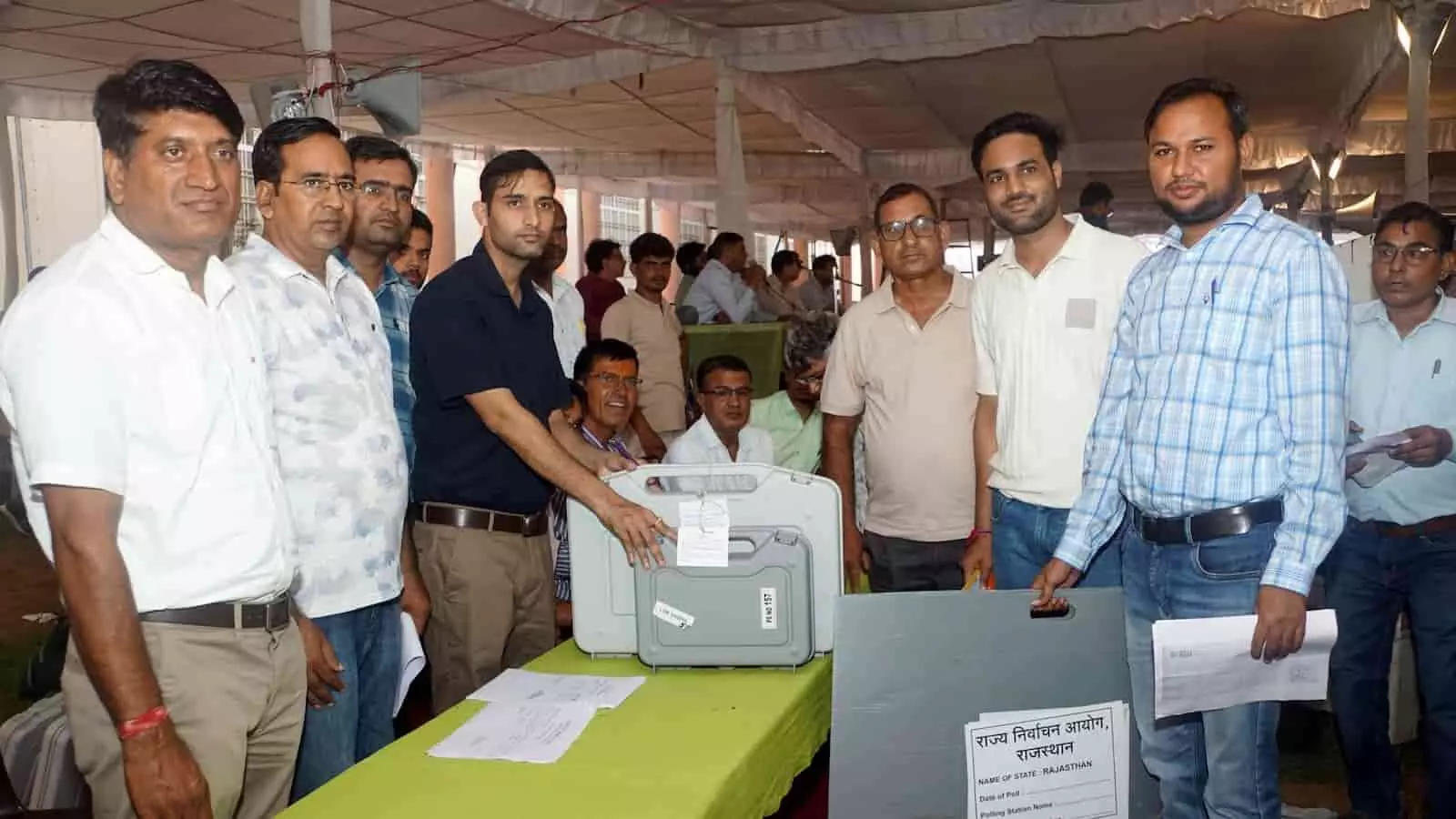 तस्वीर में चुनाव कर्मी मेज के पास खड़े होकर ईवीएम बॉक्स और निर्वाचन बोर्ड पकड़े हुए हैं। तस्वीर में चुनाव कर्मी मेज के पास खड़े होकर ईवीएम बॉक्स और निर्वाचन बोर्ड पकड़े हुए हैं।