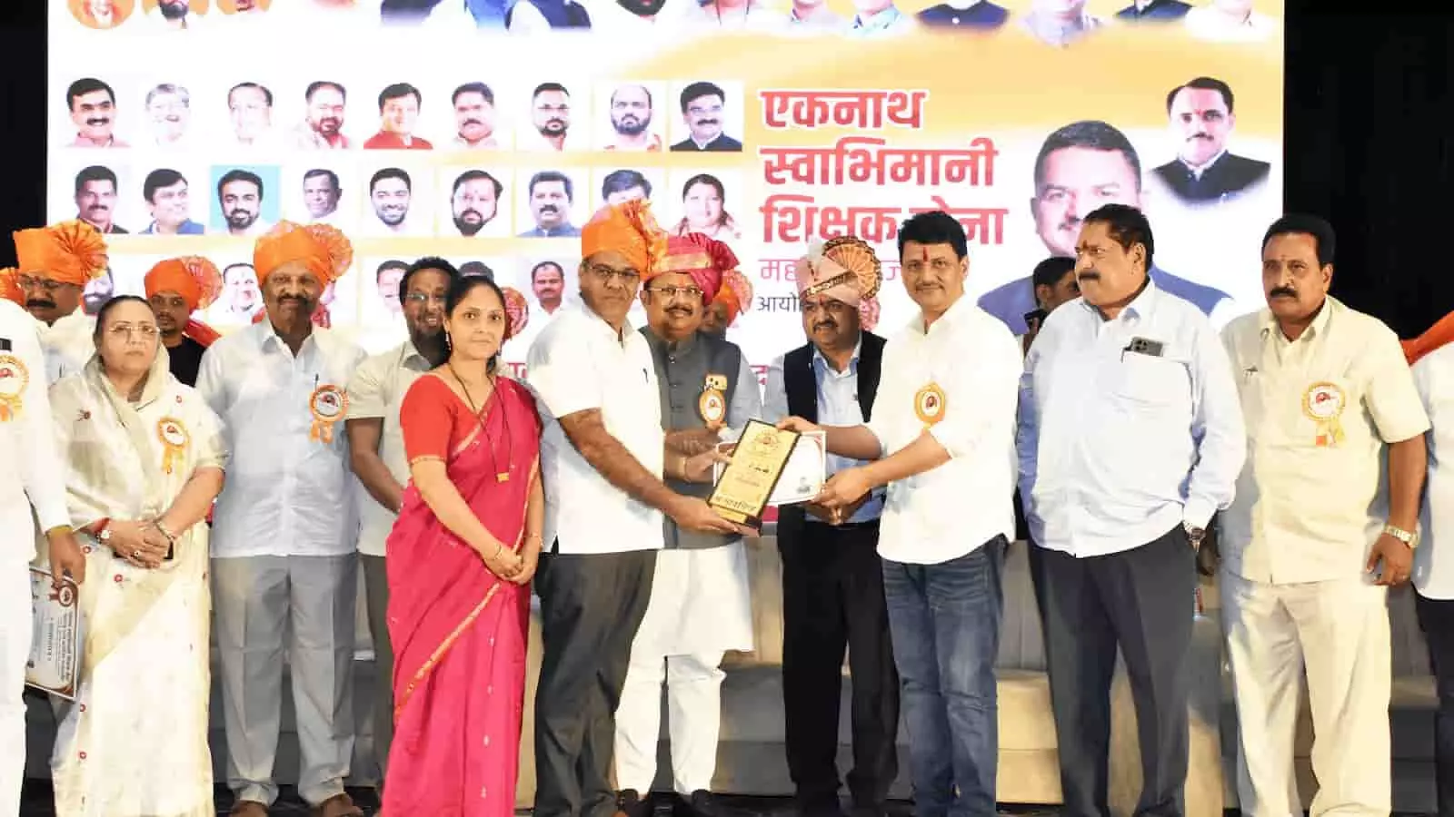 तस्वीर में बाएं से दाएं कुछ लोग खड़े हैं और बीच में अतिथियों द्वारा एक शिक्षक को प्रशस्ति पत्र और पुरस्कार प्रदान किया जा रहा है। तस्वीर में बाएं से दाएं कुछ लोग खड़े हैं और बीच में अतिथियों द्वारा एक शिक्षक को प्रशस्ति पत्र और पुरस्कार प्रदान किया जा रहा है।
