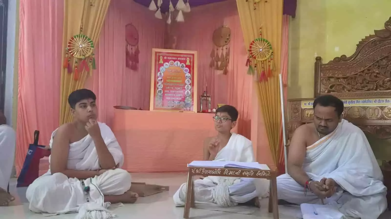 तस्वीर में बाएं से दाएं बैठे तीन आराधक हॉल में एक धार्मिक व्याख्यान के दौरान हाथ जोड़े और सुनते हुए नजर आ रहे हैं। तस्वीर में बाएं से दाएं बैठे तीन आराधक हॉल में एक धार्मिक व्याख्यान के दौरान हाथ जोड़े और सुनते हुए नजर आ रहे हैं।