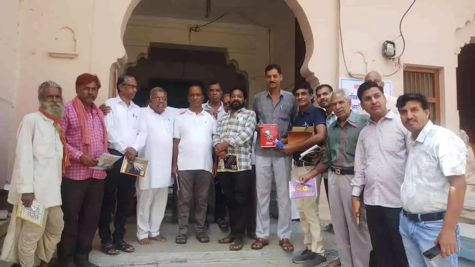 तस्वीर में दिख रही जगह पर कई लोग हाथों में किताबें लिए एक साथ खड़े हैं। तस्वीर में दिख रही जगह पर कई लोग हाथों में किताबें लिए एक साथ खड़े हैं।