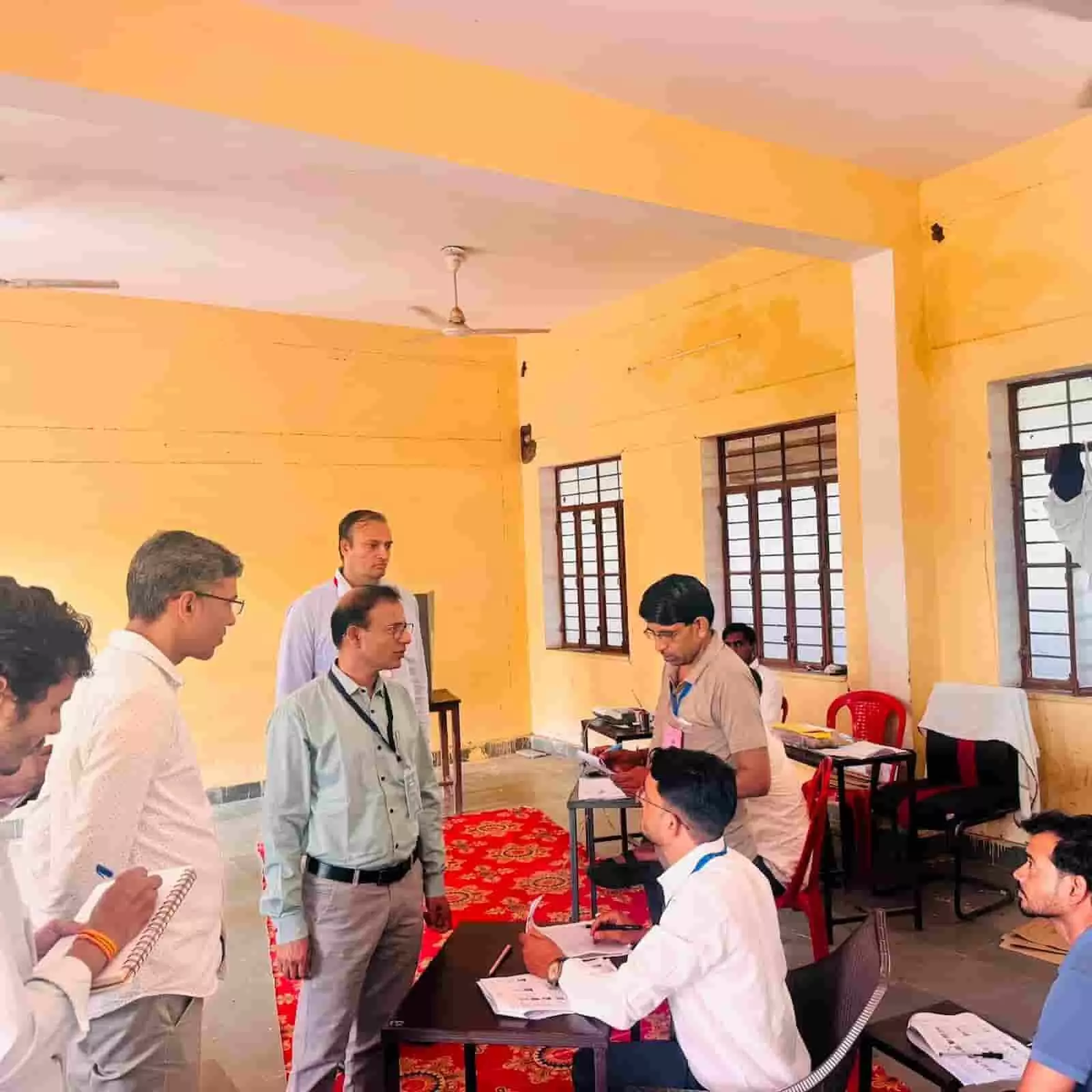 मतदान केंद्र के भीतर खड़े निर्वाचन पर्यवेक्षक टेबल पर बैठे चुनाव कार्मिकों से बातचीत कर रहे हैं। मतदान केंद्र के भीतर खड़े निर्वाचन पर्यवेक्षक टेबल पर बैठे चुनाव कार्मिकों से बातचीत कर रहे हैं।