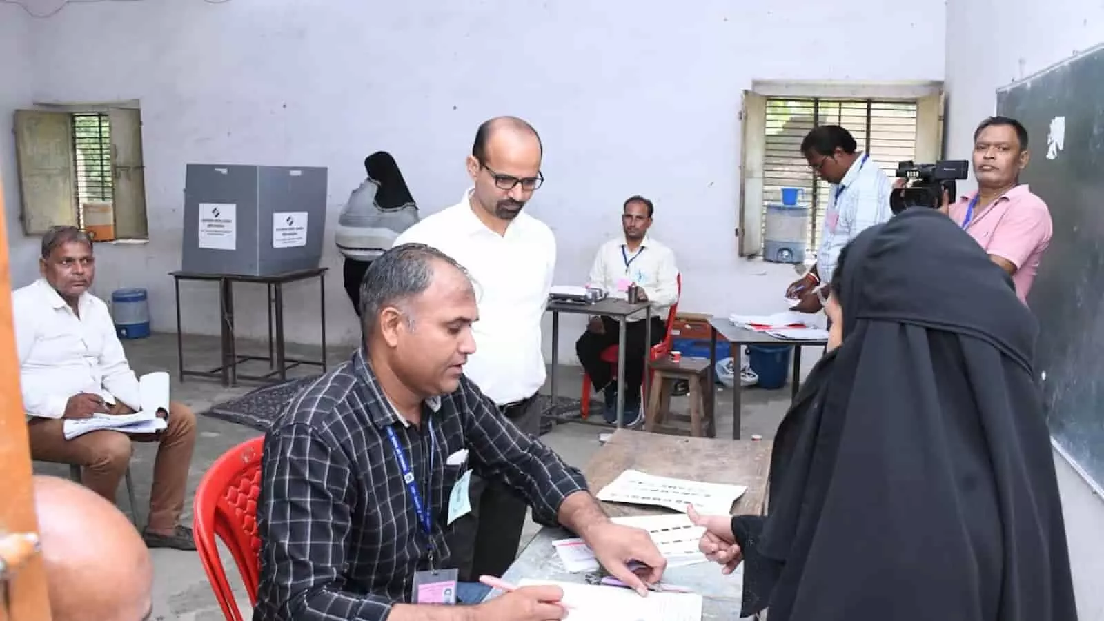 तस्वीर में मतदान केंद्र के अंदर टेबल पर बैठे पोलिंग अधिकारी मतदाता के दस्तावेज जांच रहे हैं। तस्वीर में मतदान केंद्र के अंदर टेबल पर बैठे पोलिंग अधिकारी मतदाता के दस्तावेज जांच रहे हैं।