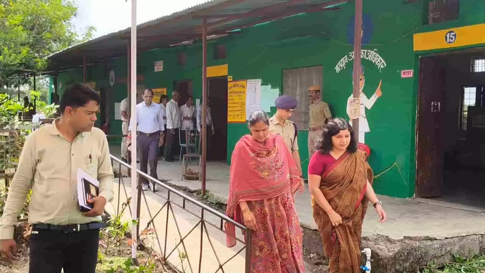 तस्वीर में मतदान केंद्र के बाहर अधिकारी और लोग दिख रहे हैं। तस्वीर में मतदान केंद्र के बाहर अधिकारी और लोग दिख रहे हैं।