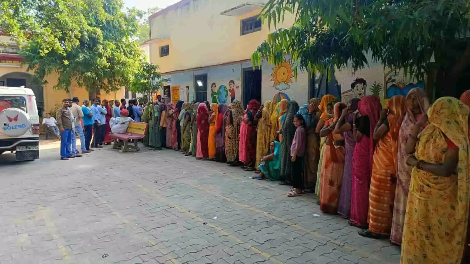 तस्वीर में एक मतदान केंद्र के बाहर महिलाओं और पुरुषों की लंबी कतार लगी हुई है, जो मतदान के लिए अपनी बारी का इंतजार कर रहे हैं। तस्वीर में एक मतदान केंद्र के बाहर महिलाओं और पुरुषों की लंबी कतार लगी हुई है, जो मतदान के लिए अपनी बारी का इंतजार कर रहे हैं।
