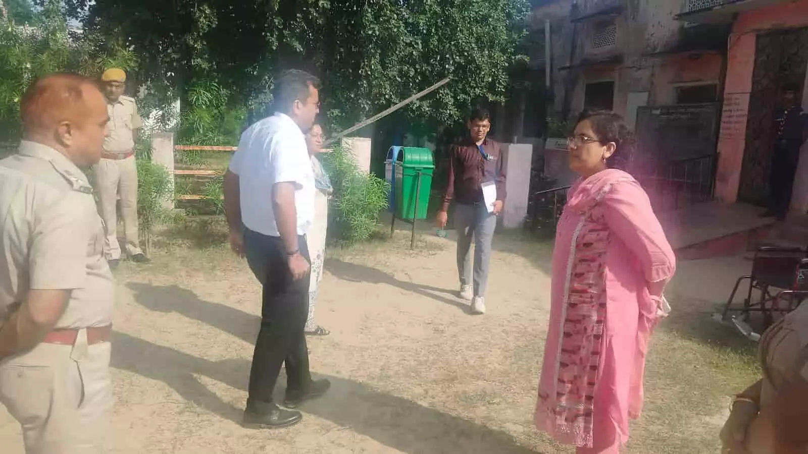 तस्वीर में एक गुलाबी सूट पहनी महिला अधिकारी और अन्य कर्मचारी बाहर परिसर में खड़े नजर आ रहे हैं। तस्वीर में एक गुलाबी सूट पहनी महिला अधिकारी और अन्य कर्मचारी बाहर परिसर में खड़े नजर आ रहे हैं।