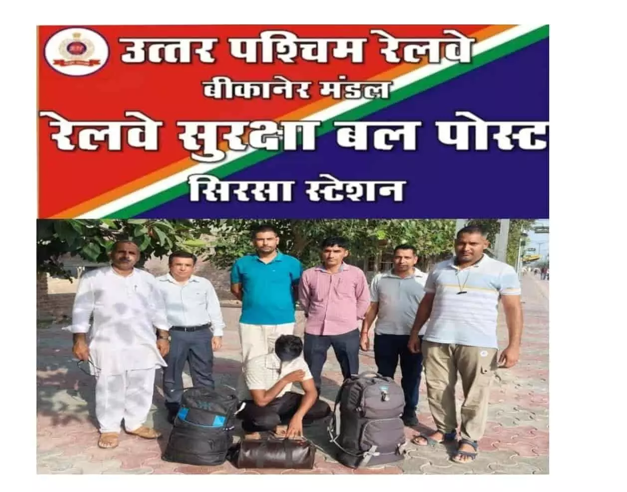 तस्वीर में बाएं से दाएं खड़े छह लोग, जमीन पर बैठे एक व्यक्ति और उसके पास रखे तीन बैग दिख रहे हैं। तस्वीर में बाएं से दाएं खड़े छह लोग, जमीन पर बैठे एक व्यक्ति और उसके पास रखे तीन बैग दिख रहे हैं।