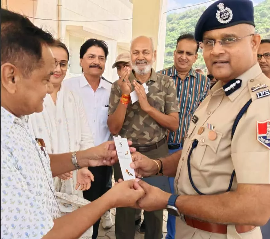 तस्वीर में पुलिस की वर्दी पहने एक अधिकारी और अन्य लोग आपस में कागज या पर्चा थामे हुए खड़े हैं। तस्वीर में पुलिस की वर्दी पहने एक अधिकारी और अन्य लोग आपस में कागज या पर्चा थामे हुए खड़े हैं।