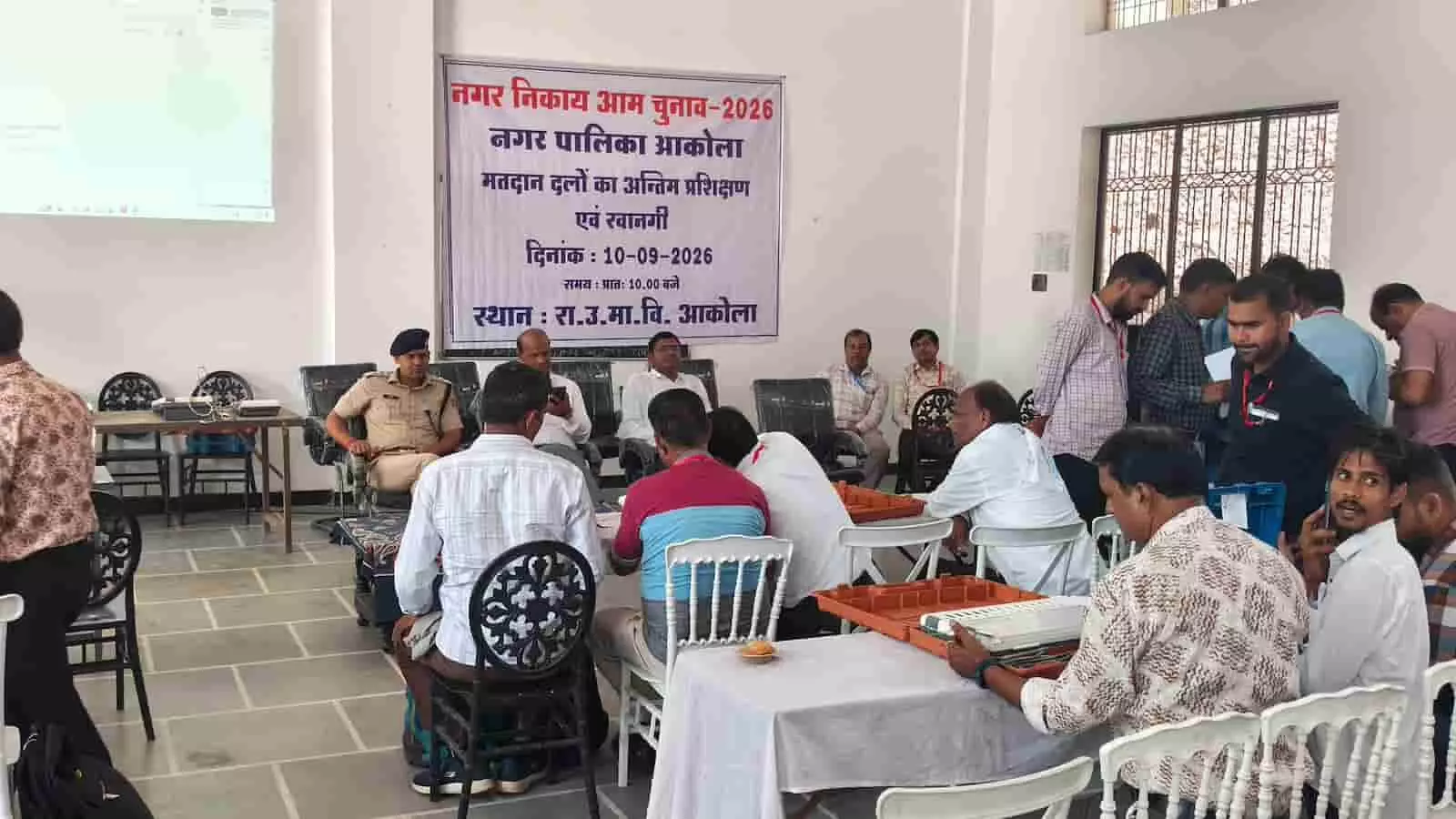 तस्वीर में बायीं ओर से दाईं ओर कई लोग और पुलिसकर्मी हॉल में कुर्सियों पर बैठे और खड़े दिखाई दे रहे हैं। तस्वीर में बायीं ओर से दाईं ओर कई लोग और पुलिसकर्मी हॉल में कुर्सियों पर बैठे और खड़े दिखाई दे रहे हैं।