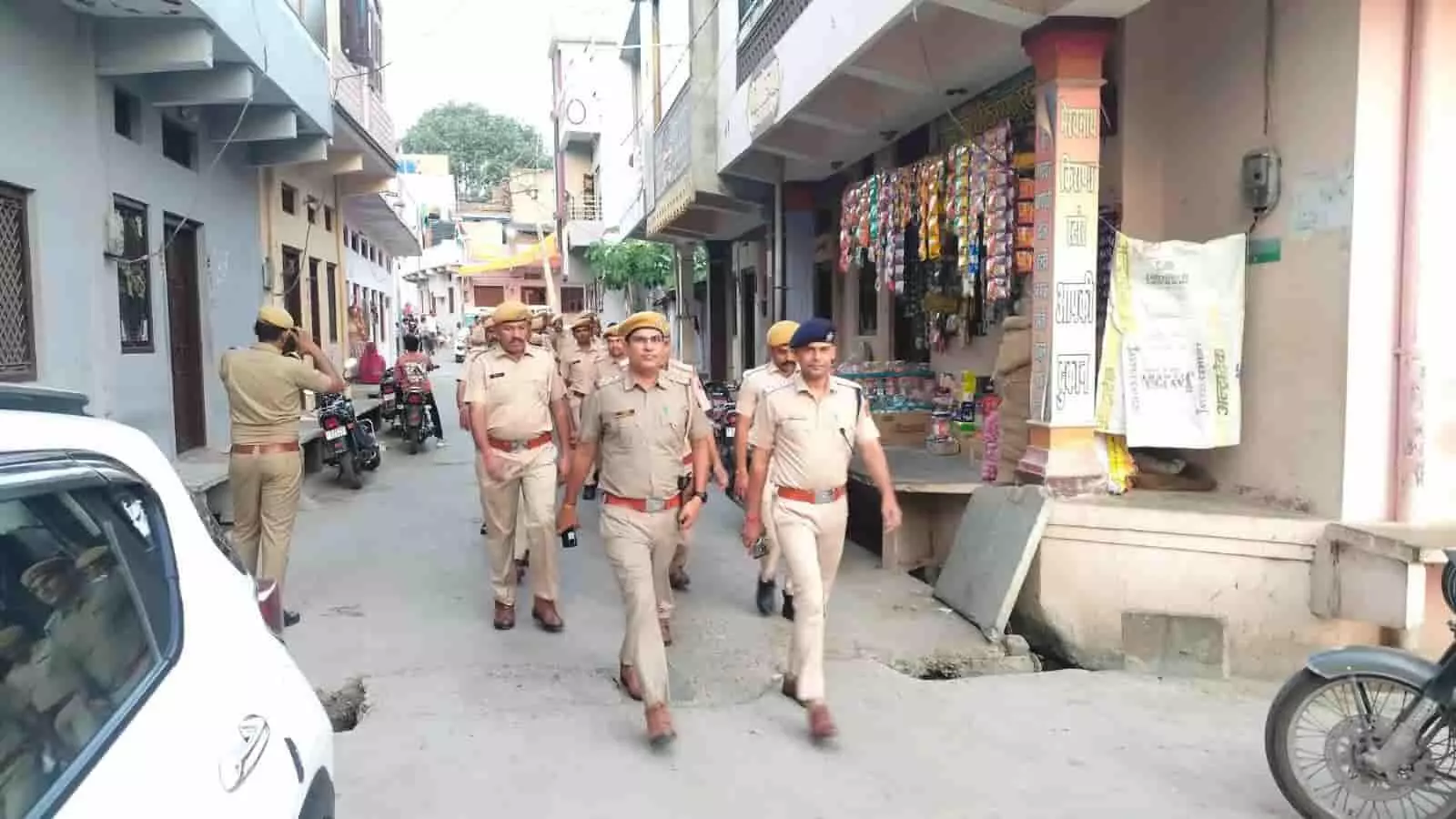 तस्वीर में खाकी वर्दी पहने कई पुलिसकर्मी और अधिकारी एक संकरी गली में आगे की ओर पैदल चलते नजर आ रहे हैं। तस्वीर में खाकी वर्दी पहने कई पुलिसकर्मी और अधिकारी एक संकरी गली में आगे की ओर पैदल चलते नजर आ रहे हैं।