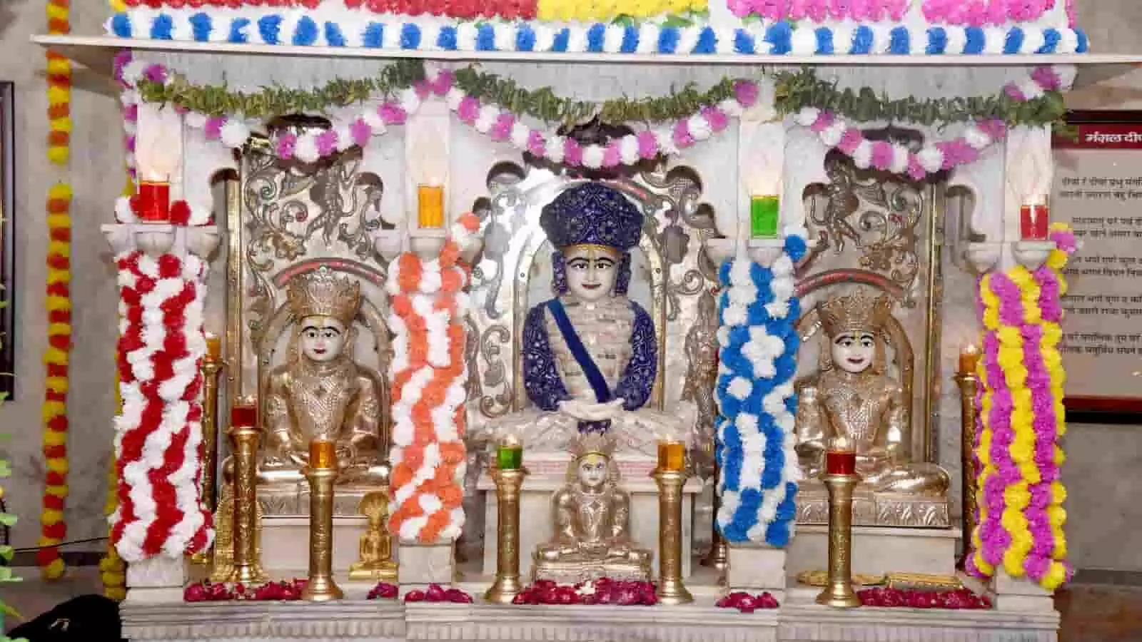 तस्वीर में सफेद और सुनहरी जैन प्रतिमाएं सजावट और फूलों से घिरे मंदिर के गर्भगृह में विराजमान हैं। तस्वीर में सफेद और सुनहरी जैन प्रतिमाएं सजावट और फूलों से घिरे मंदिर के गर्भगृह में विराजमान हैं।