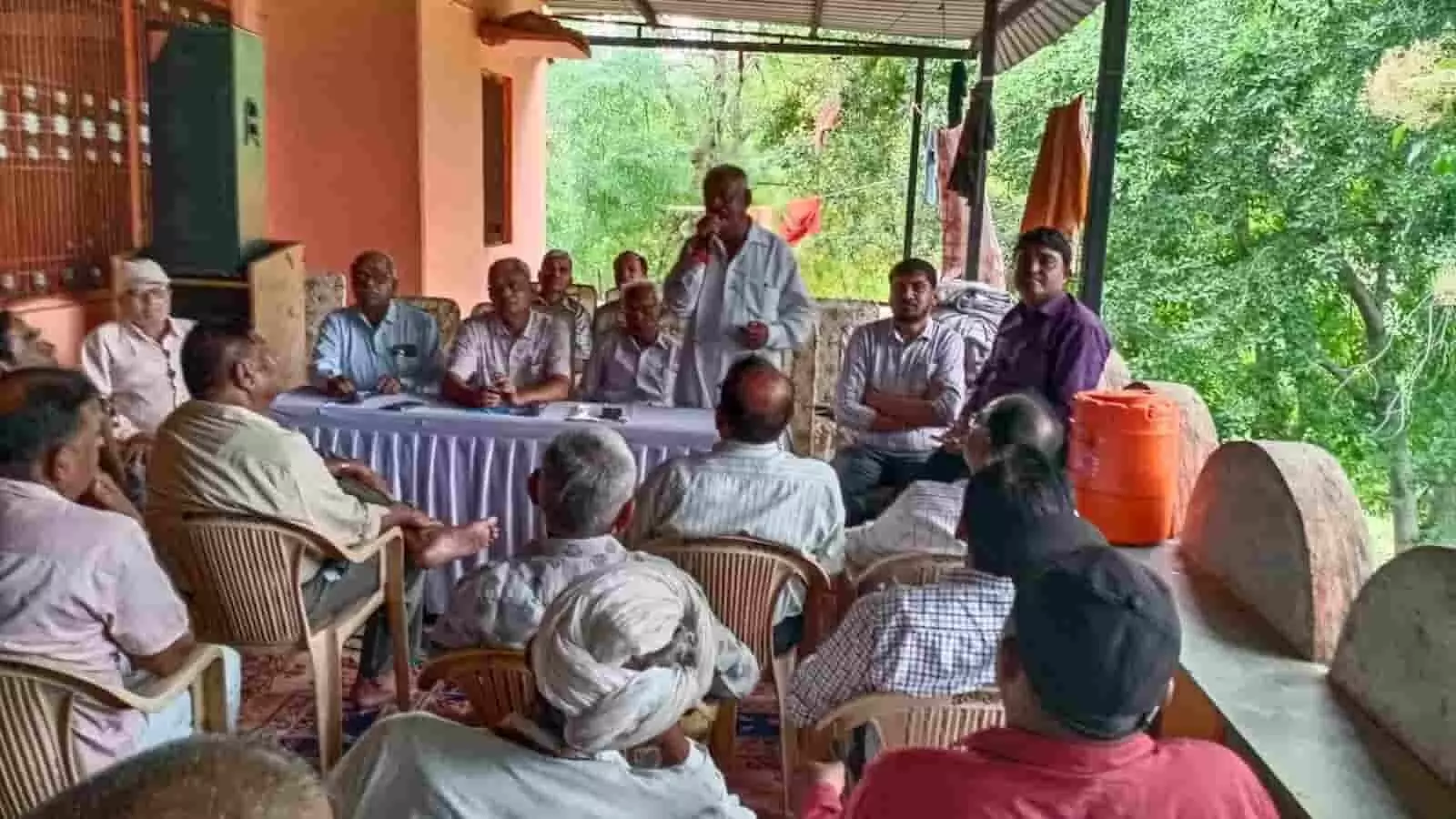 तस्वीर में दिख रही बैठक में एक व्यक्ति माइक पर संबोधित कर रहा है और लोग बैठे सुन रहे हैं। तस्वीर में दिख रही बैठक में एक व्यक्ति माइक पर संबोधित कर रहा है और लोग बैठे सुन रहे हैं।