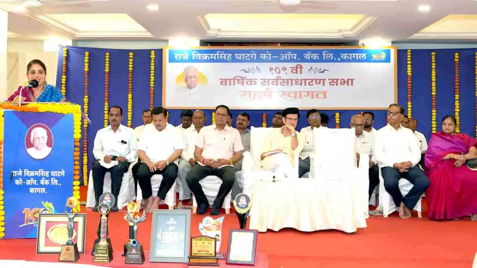 तस्वीर में पोडियम पर नवोदिता घाटगे भाषण दे रही हैं और मंच पर समरजितसिंह घाटगे तथा अन्य निदेशक बैठे हैं। तस्वीर में पोडियम पर नवोदिता घाटगे भाषण दे रही हैं और मंच पर समरजितसिंह घाटगे तथा अन्य निदेशक बैठे हैं।