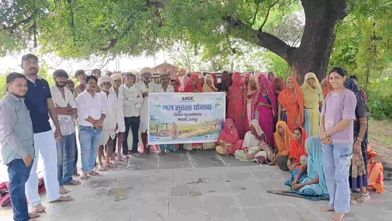 तस्वीर में बीका खेड़ा गांव में पेड़ के नीचे खड़े पुरुष, बैठी महिलाएं और जल सुरक्षा योजना का बैनर दिखाई दे रहा है। तस्वीर में बीका खेड़ा गांव में पेड़ के नीचे खड़े पुरुष, बैठी महिलाएं और जल सुरक्षा योजना का बैनर दिखाई दे रहा है।