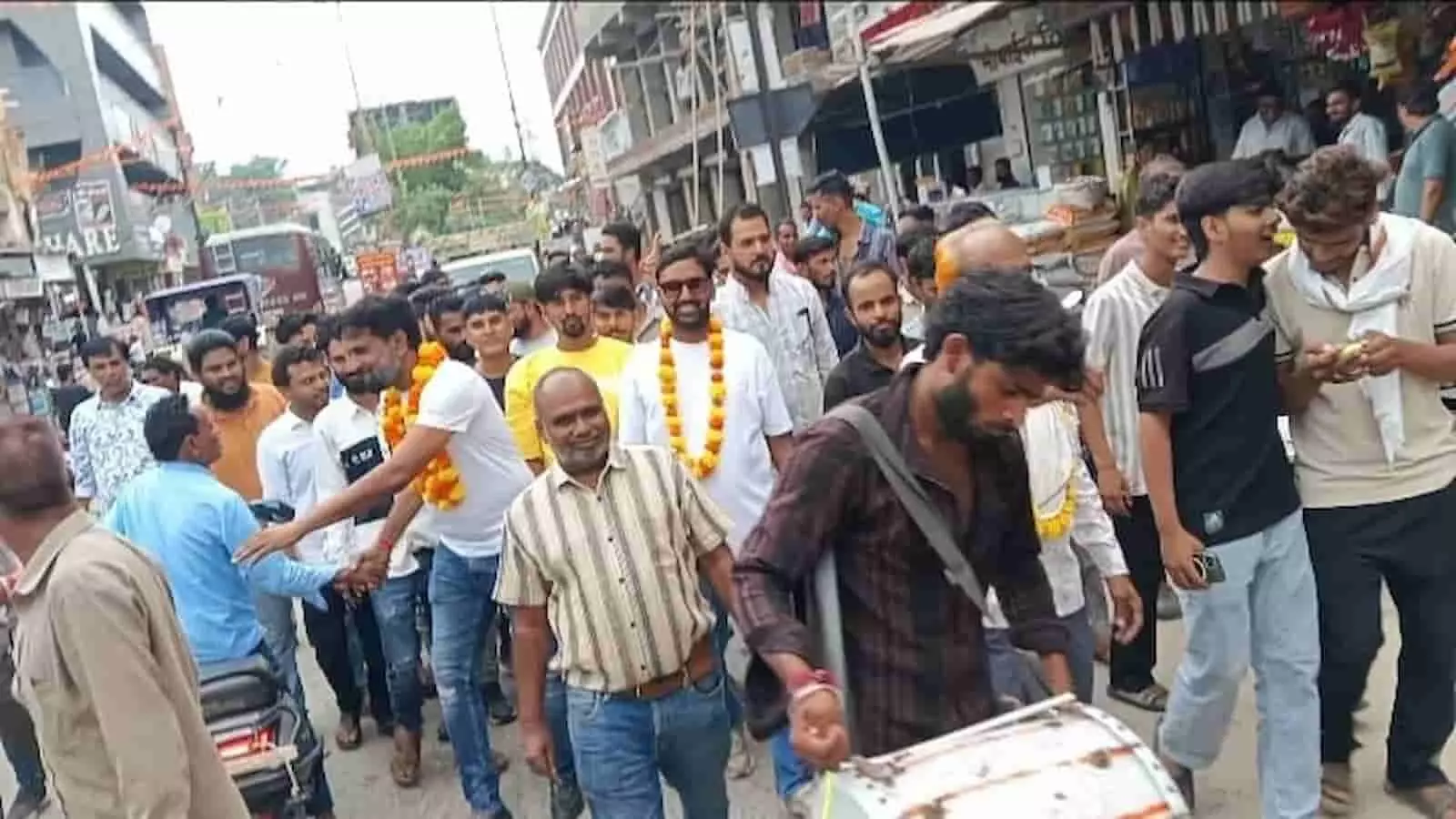 तस्वीर में गंगापुर की सड़क पर जुलूस के दौरान हाथों में माला पहने लोग और आगे ड्रम बजाता हुआ एक व्यक्ति दिखाई दे रहा है तस्वीर में गंगापुर की सड़क पर जुलूस के दौरान हाथों में माला पहने लोग और आगे ड्रम बजाता हुआ एक व्यक्ति दिखाई दे रहा है