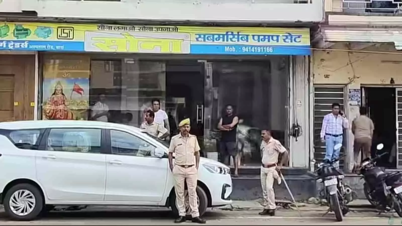 तस्वीर में दुकान के सामने एक सफेद कार खड़ी है और पुलिसकर्मी पहरा देते हुए दिखाई दे रहे हैं। तस्वीर में दुकान के सामने एक सफेद कार खड़ी है और पुलिसकर्मी पहरा देते हुए दिखाई दे रहे हैं।