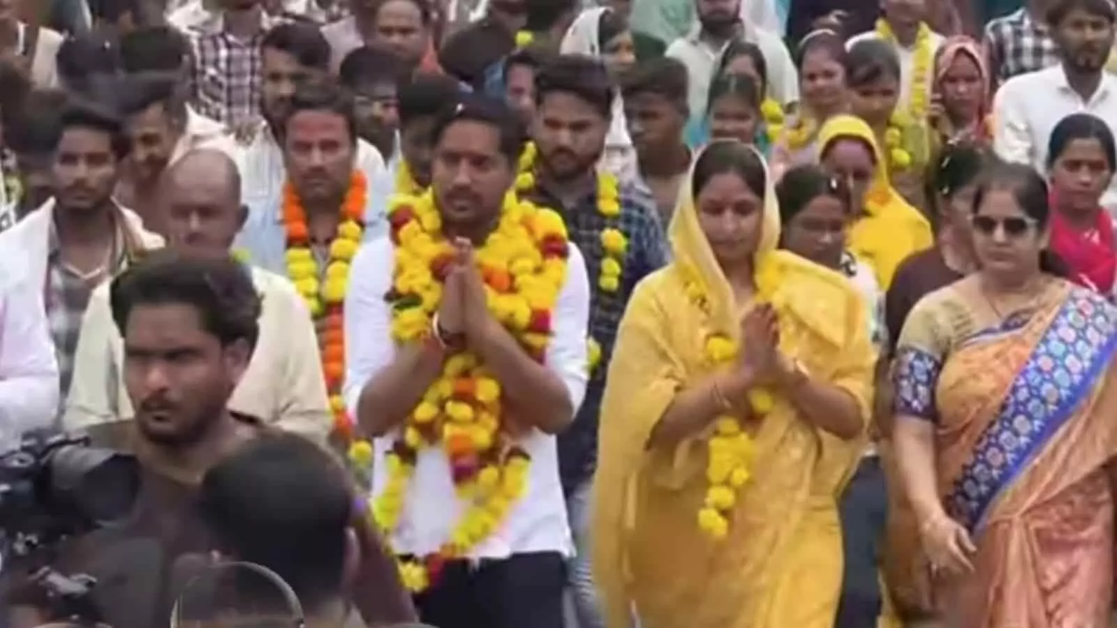 तस्वीर में आगे पीले कपड़ों में महिलाएं और गले में माला पहने लोग सड़क पर चलते हुए दिखाई दे रहे हैं। तस्वीर में आगे पीले कपड़ों में महिलाएं और गले में माला पहने लोग सड़क पर चलते हुए दिखाई दे रहे हैं।
