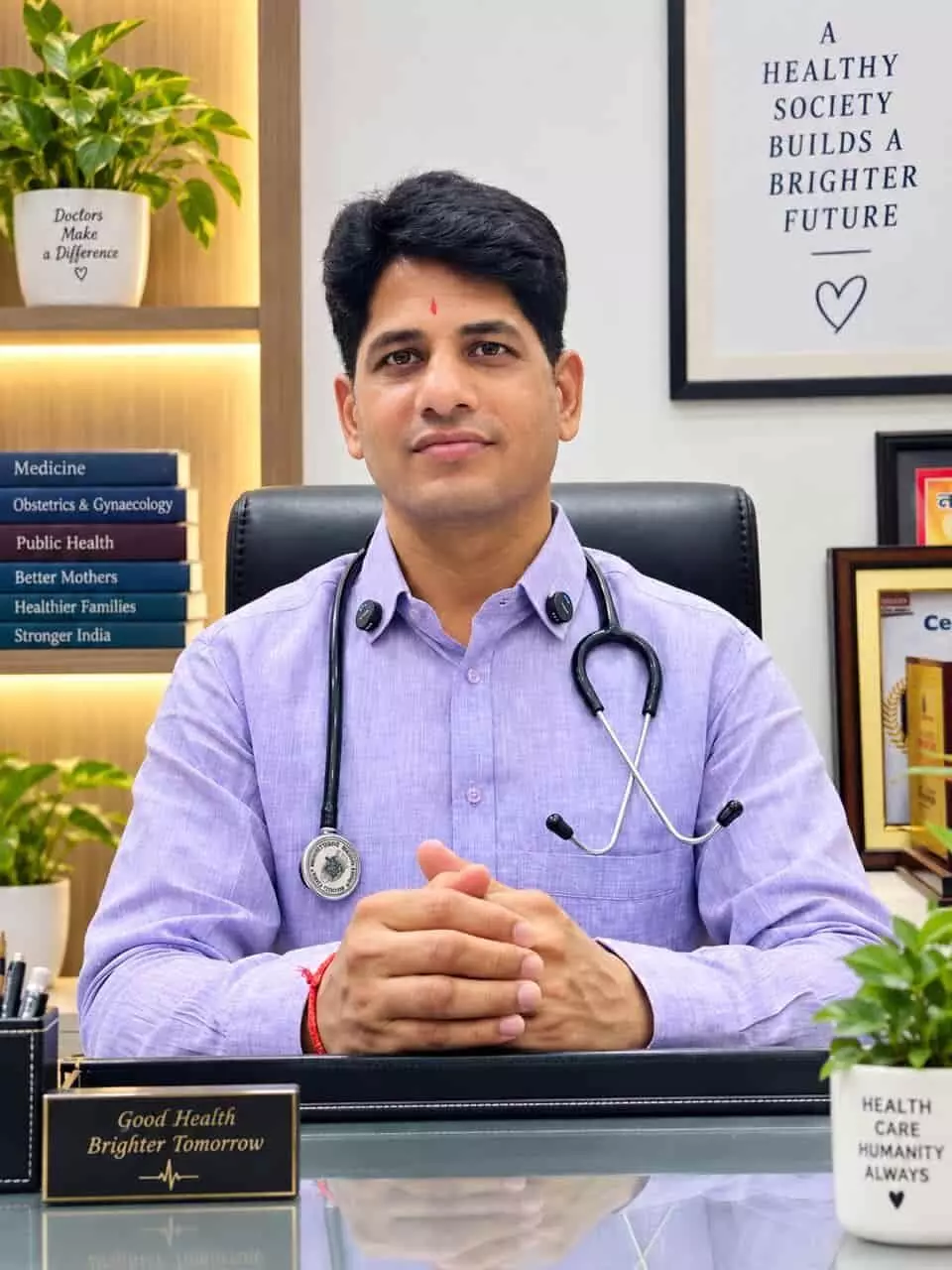 तस्वीर में पर्पल शर्ट पहने और गले में स्टेथोस्कोप लटकाए हुए एक डॉक्टर मेज के पास बैठे हुए दिखाई दे रहे हैं। तस्वीर में पर्पल शर्ट पहने और गले में स्टेथोस्कोप लटकाए हुए एक डॉक्टर मेज के पास बैठे हुए दिखाई दे रहे हैं।
