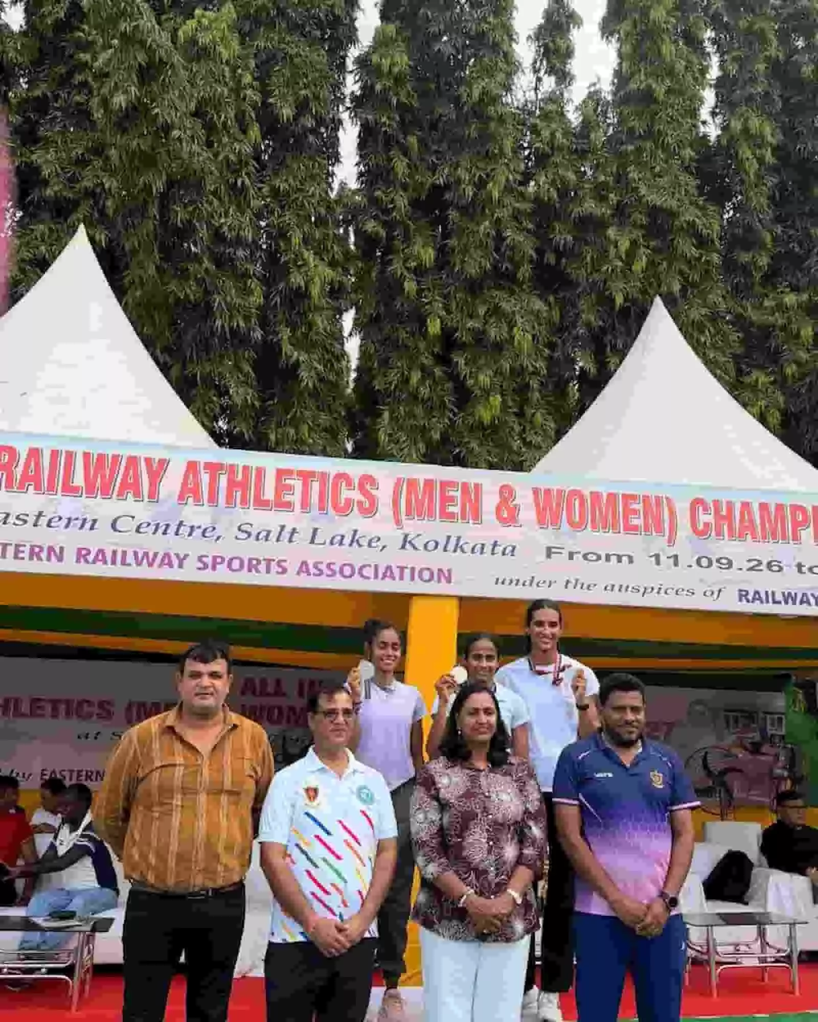 तस्वीर में दिख रही महिला एथलीट मंच पर अपने पदक प्रदर्शित कर रही हैं और अधिकारी आगे खड़े हैं। तस्वीर में दिख रही महिला एथलीट मंच पर अपने पदक प्रदर्शित कर रही हैं और अधिकारी आगे खड़े हैं।
