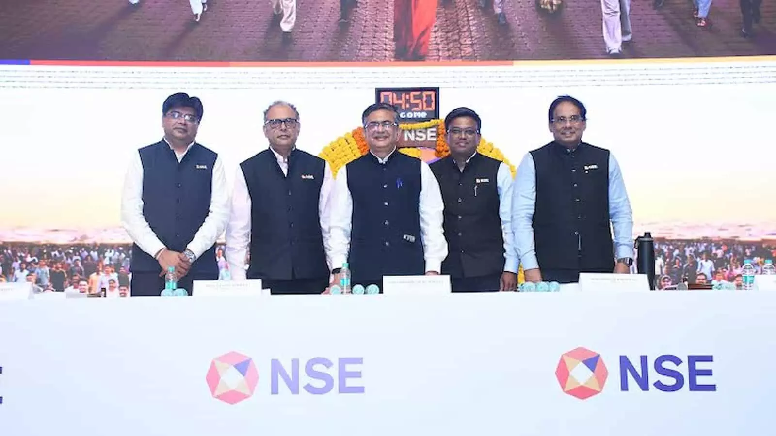 तस्वीर में पांच अधिकारी मंच पर खड़े हैं और उनके आगे एनएसई का लोगो लगा है। तस्वीर में पांच अधिकारी मंच पर खड़े हैं और उनके आगे एनएसई का लोगो लगा है।