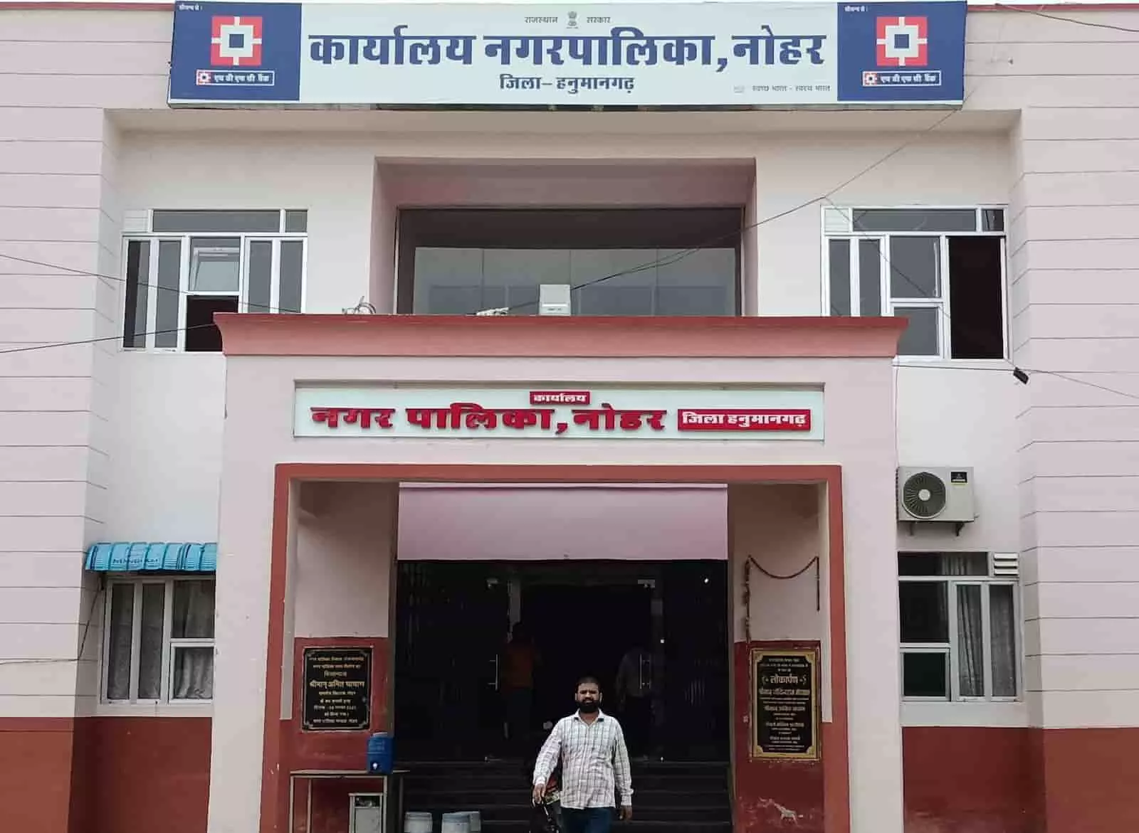 तस्वीर में नोहर नगर पालिका कार्यालय की दो मंजिला इमारत और उसके मुख्य द्वार का दृश्य। तस्वीर में नोहर नगर पालिका कार्यालय की दो मंजिला इमारत और उसके मुख्य द्वार का दृश्य।