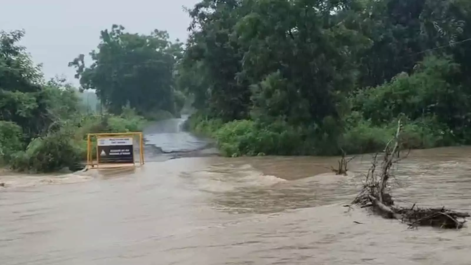 तस्वीर में सड़क पर पुल के ऊपर से बहता हुआ पानी और आसपास हरियाली दिखाई दे रही है। तस्वीर में सड़क पर पुल के ऊपर से बहता हुआ पानी और आसपास हरियाली दिखाई दे रही है।